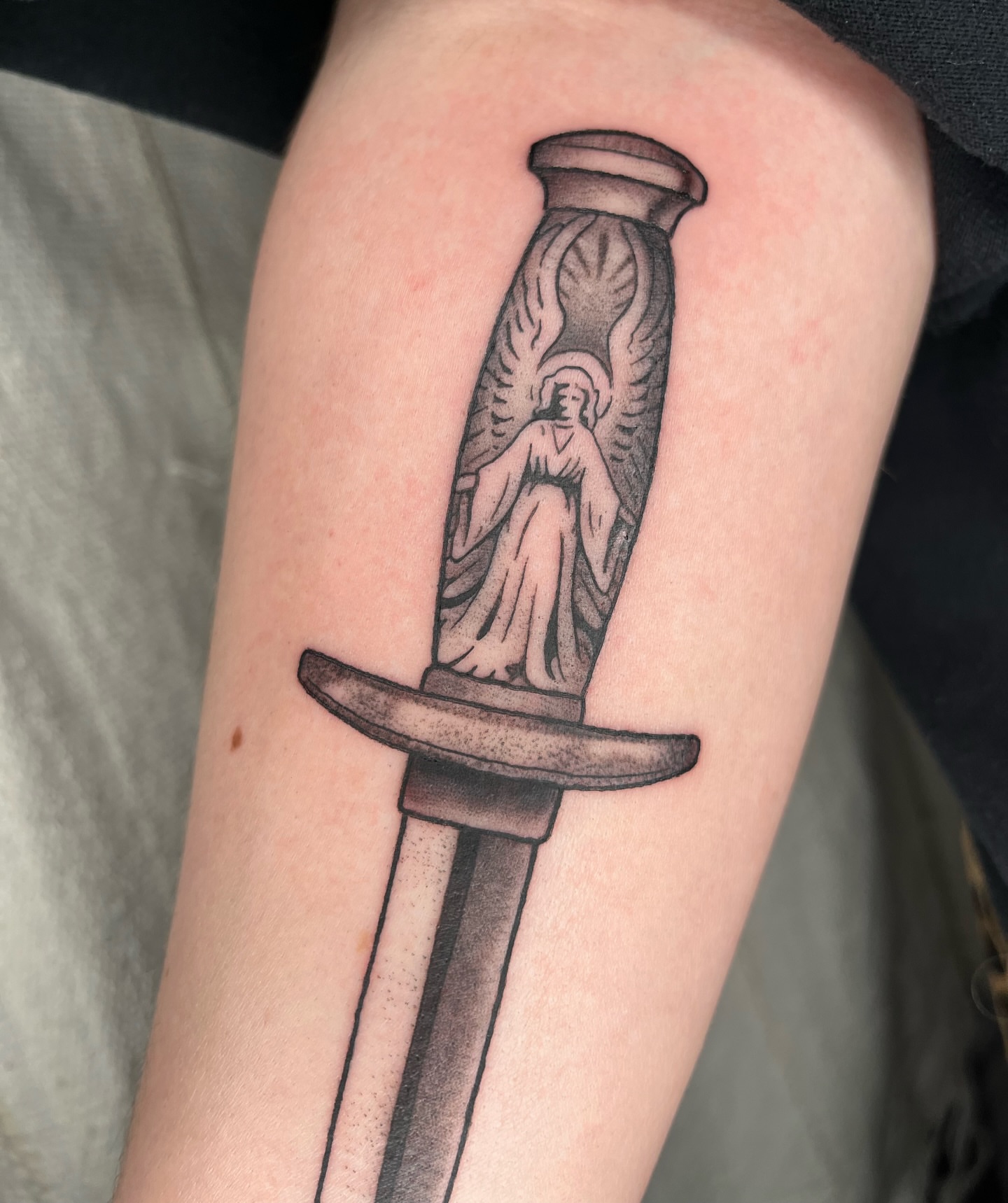 Angelic figure within sword black and grey tattoo on the forearm by Maris Hare, Philadelphia, Pennsylvania