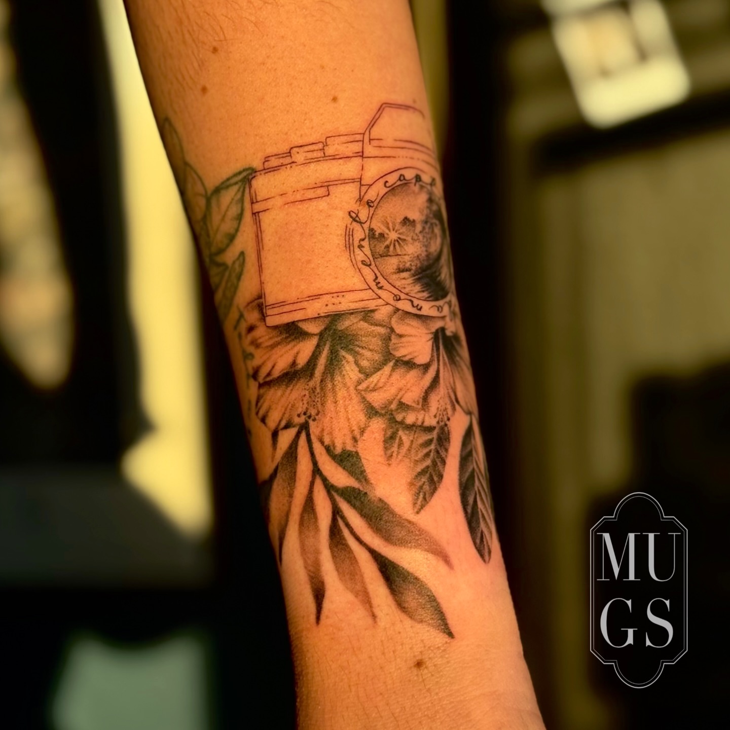 Camera and floral realism tattoo on the forearm by Emily Andreozzi