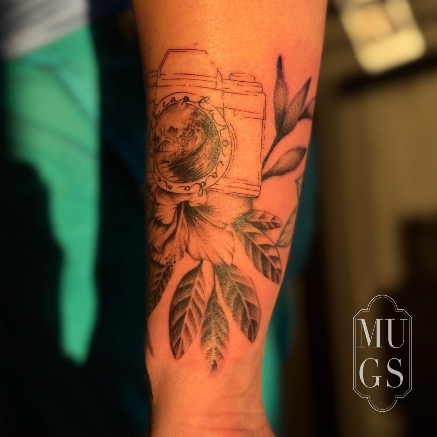 Camera and leaves black and grey tattoo on the forearm by Emily Andreozzi