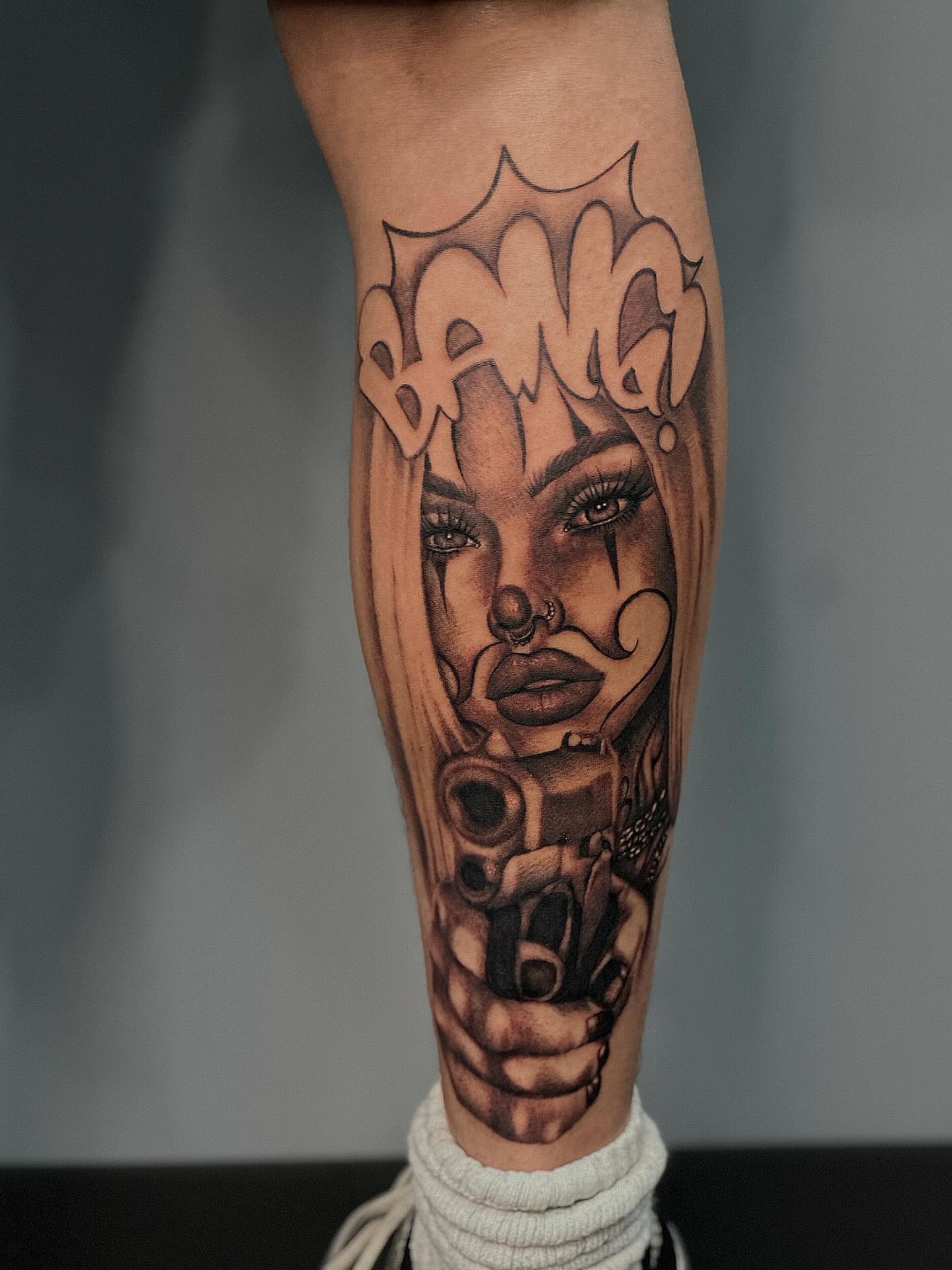 Woman with gun black and grey tattoo on the forearm by Lissy Red