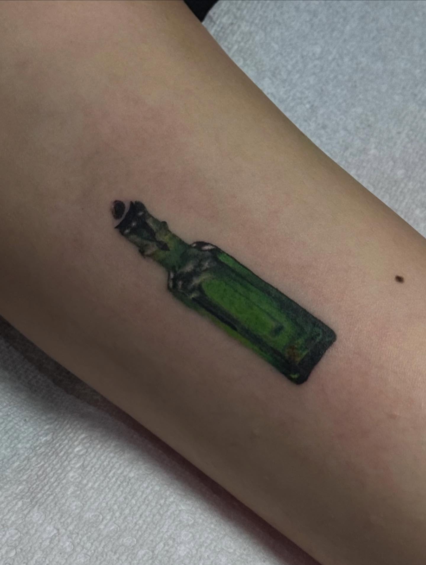 Green bottle realism tattoo on the forearm by Nat🫧