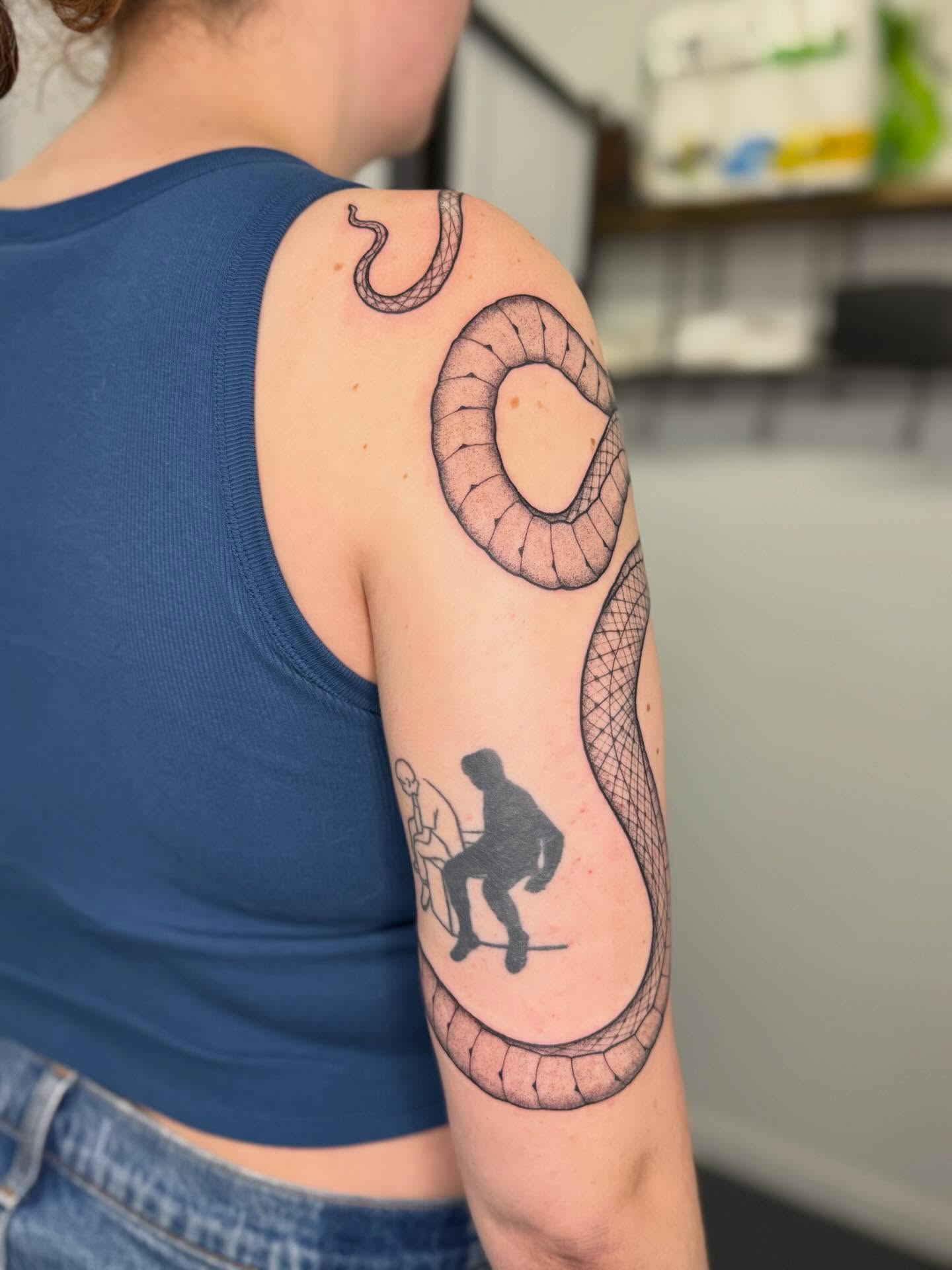 Snake and figure black and grey tattoo on the upper arm by Noelle Adrienne Tattoos