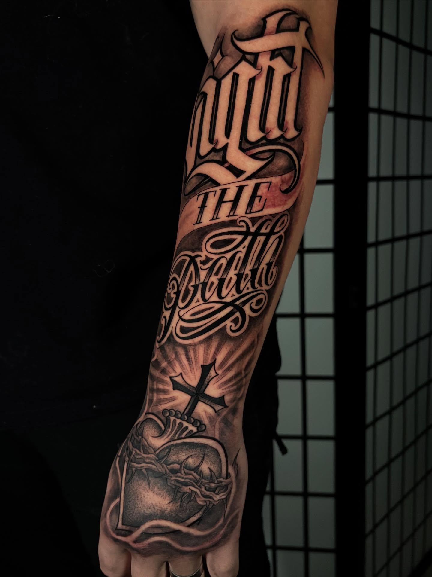 Heart with cross black and grey tattoo on the forearm by Trusty Dizon Tattoo Artist