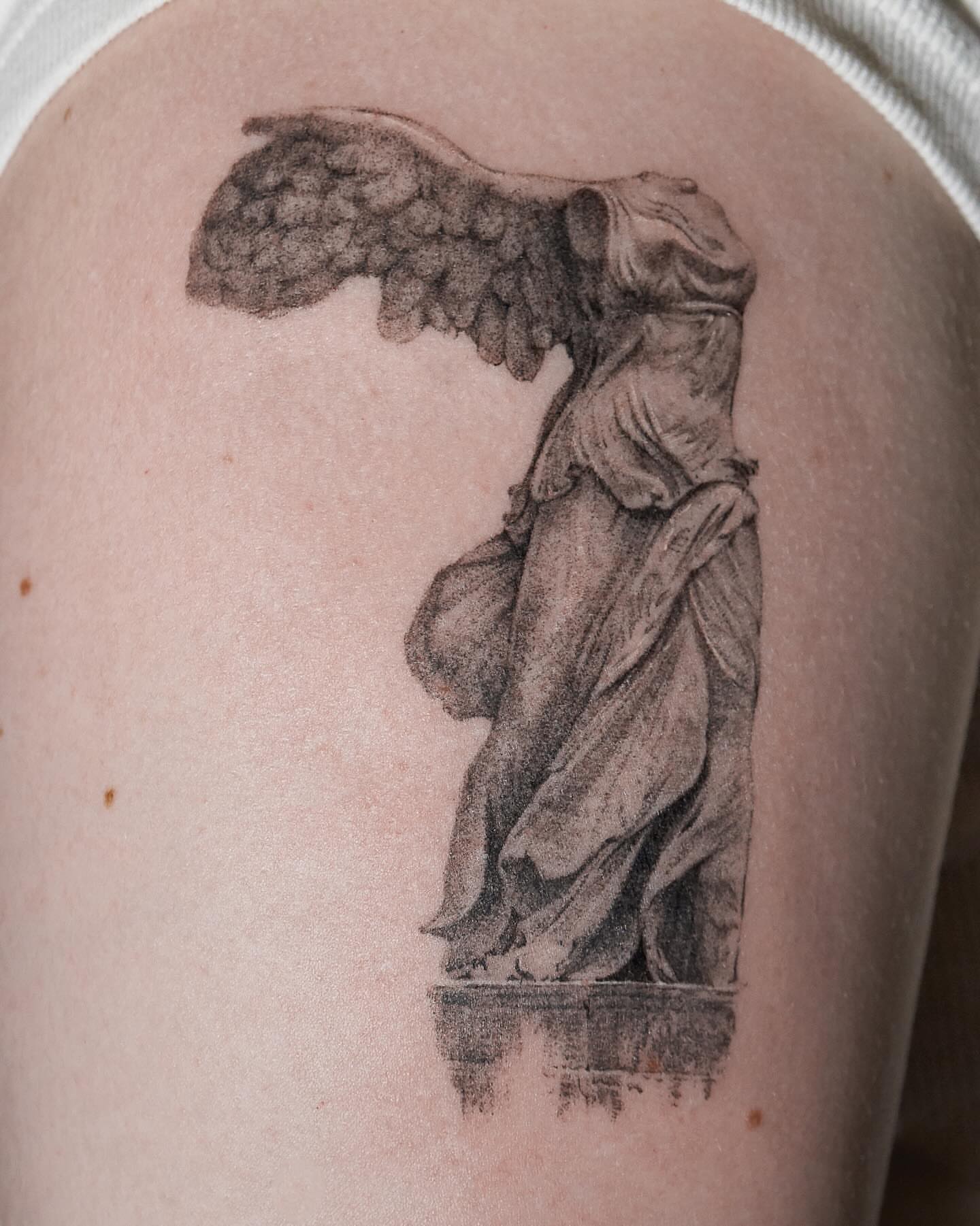 Winged statue black and grey tattoo on the upper arm by Tattoo artist LA ། Fine line, Micro realism