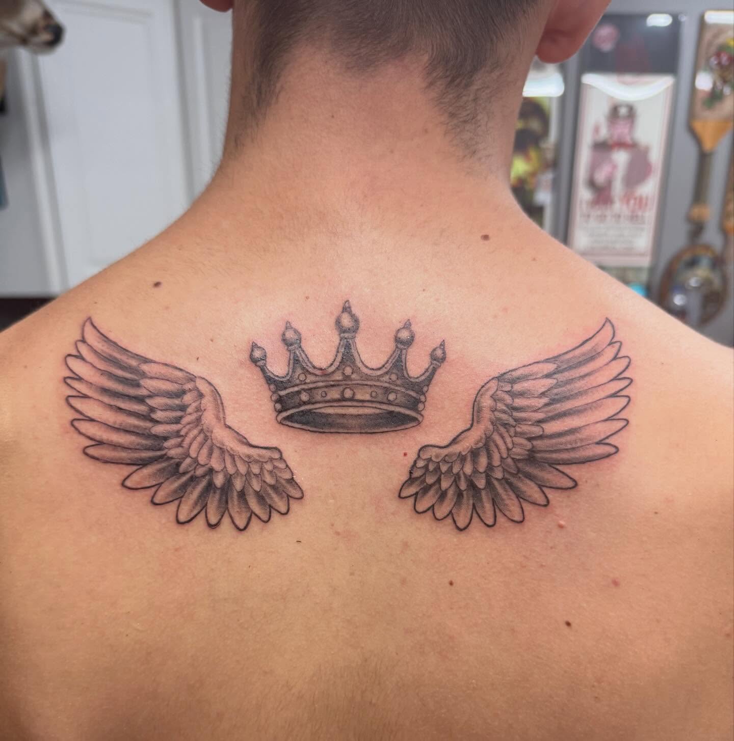 Wings and crown black and grey tattoo on the back by Daniel Smith