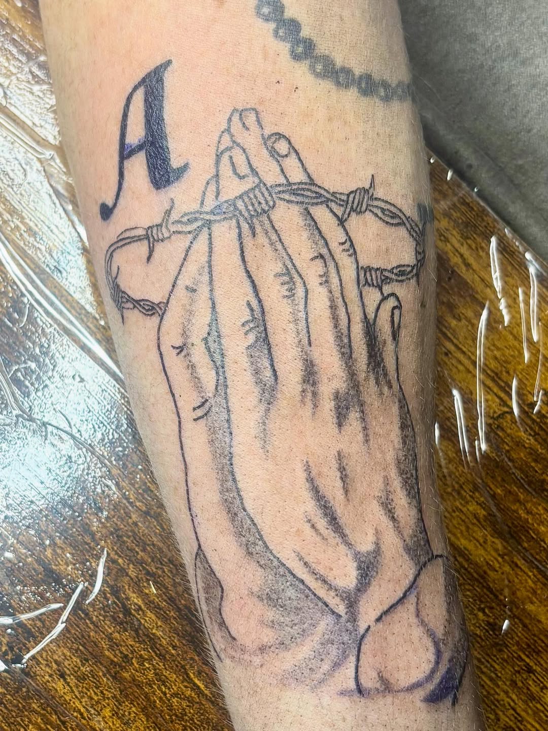 Praying hands with barbed wire sketch tattoo on the forearm by sams tattoos