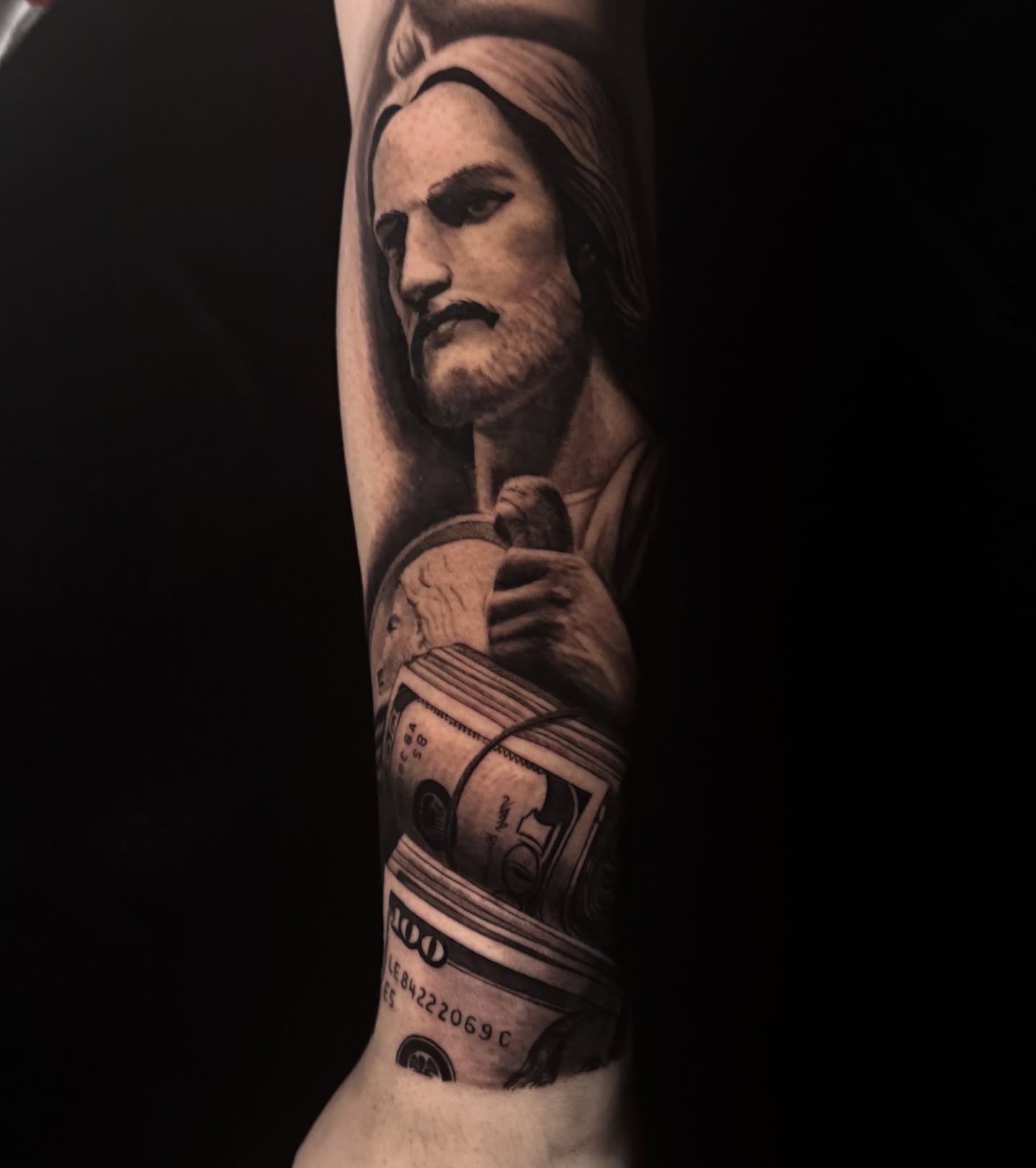 Religious figure with money realism tattoo on the forearm by Elian Sanchez Austin Tx. Tattoo Artist