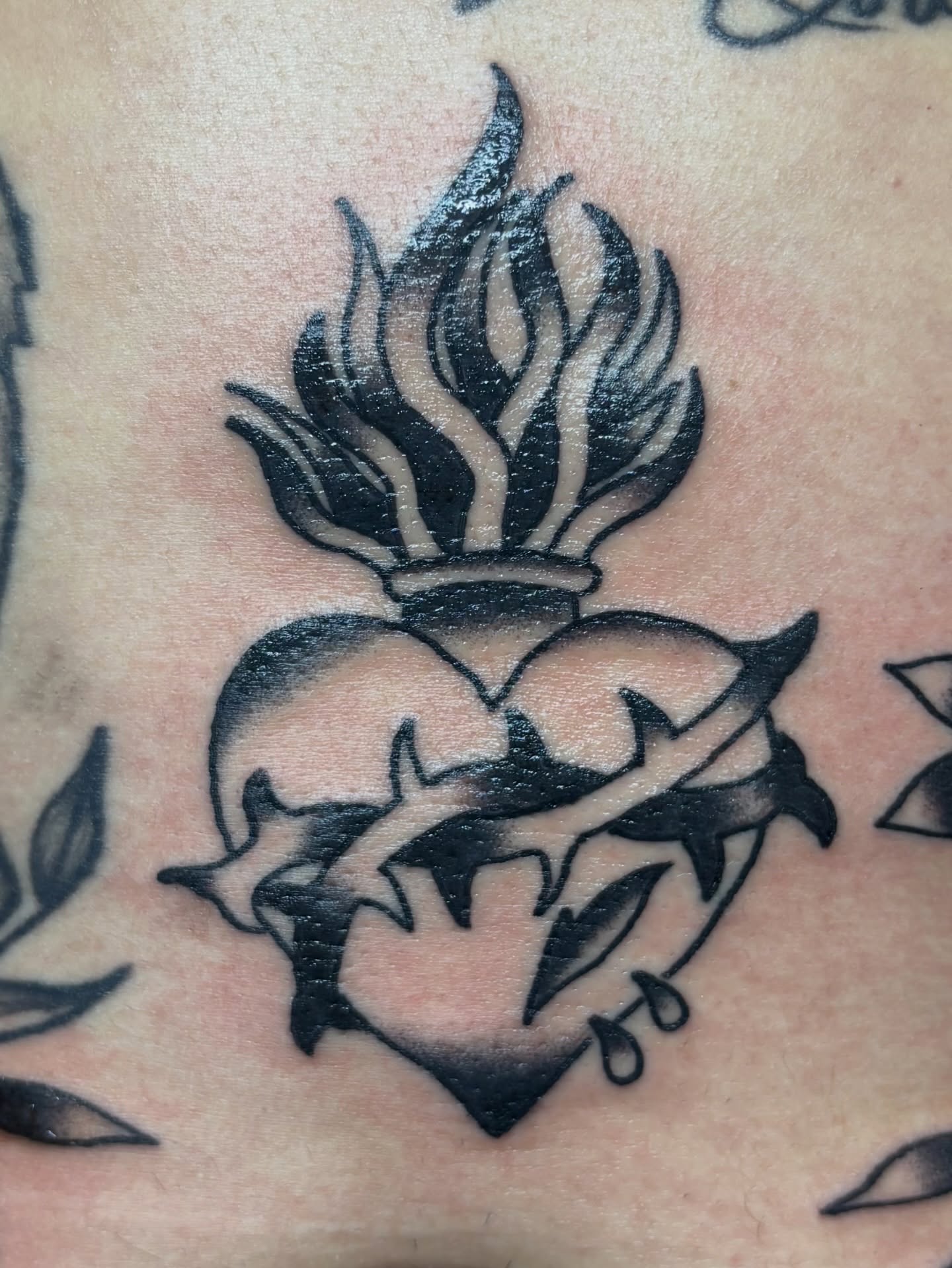 Broken heart with flames black and grey tattoo on the chest by Bridget Smith