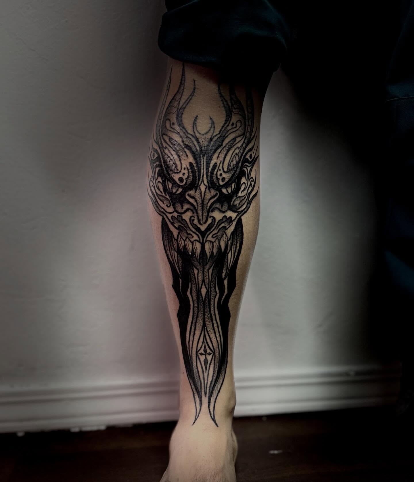 Mask black and grey tattoo on the calf by Sasha “Sashimi” Shabasov