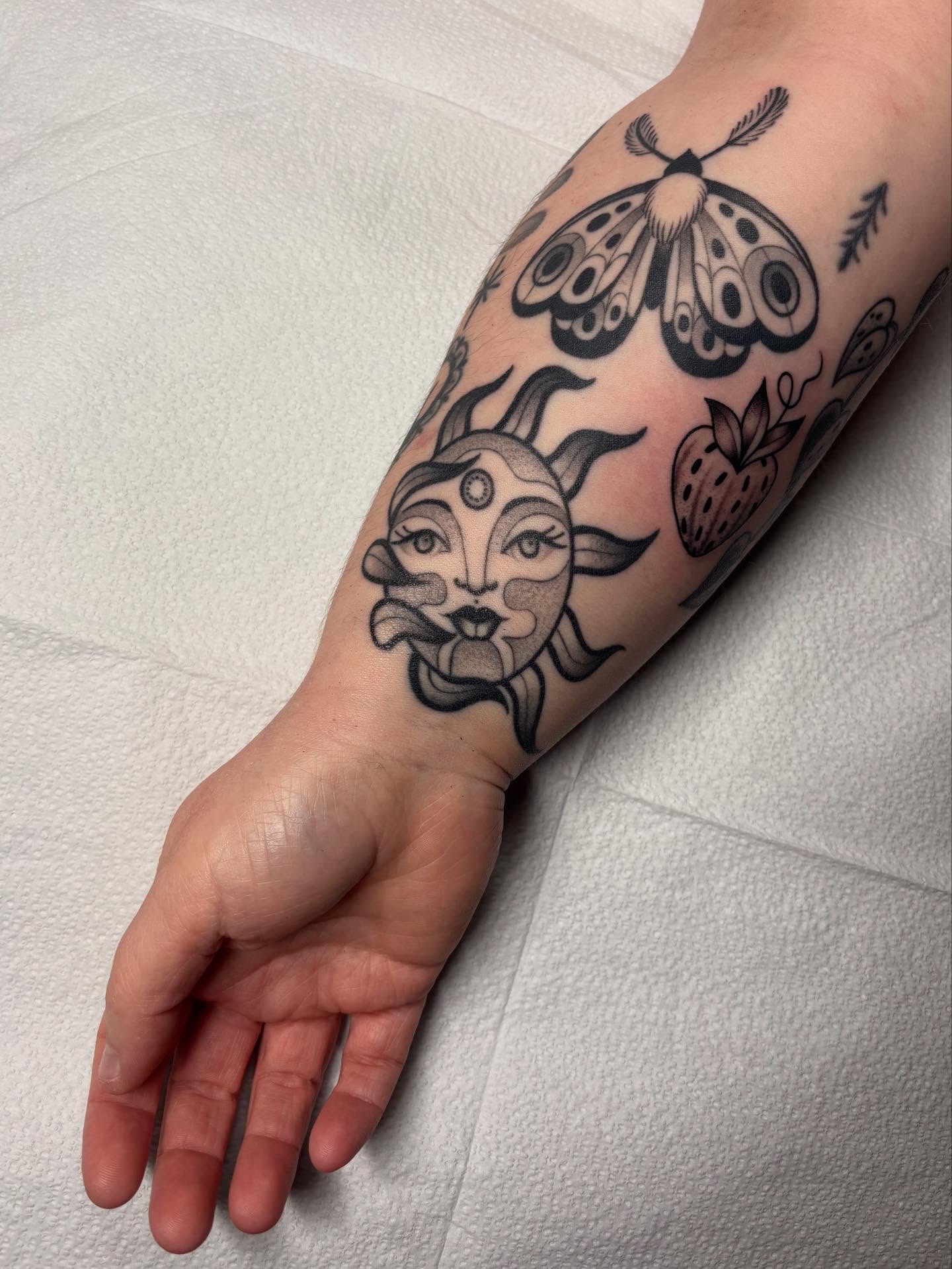 Sun and moth black and grey tattoo on the forearm by Victoria Bacon