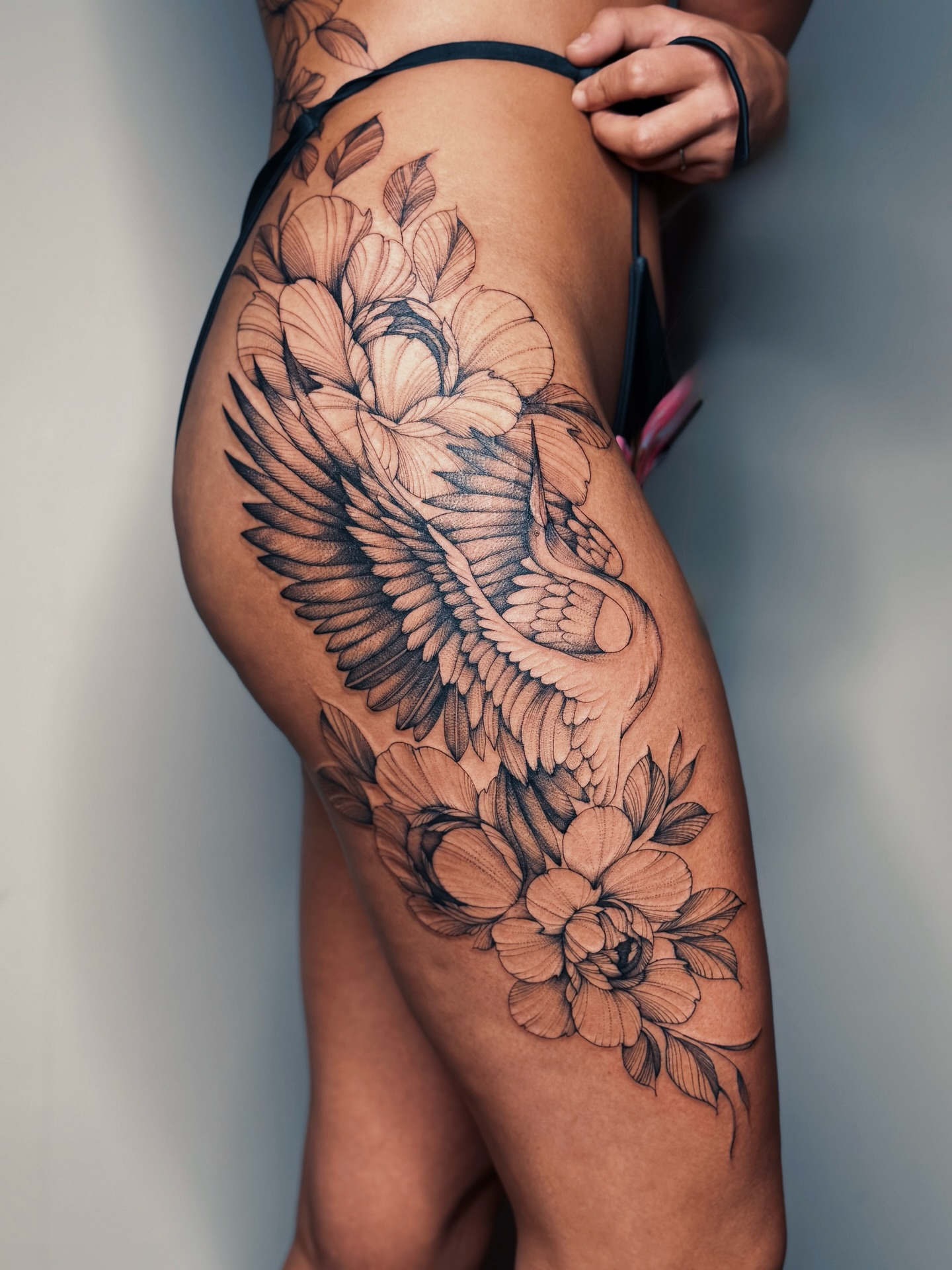Swan and flowers black and grey tattoo on the thigh by Olha Tytarenko