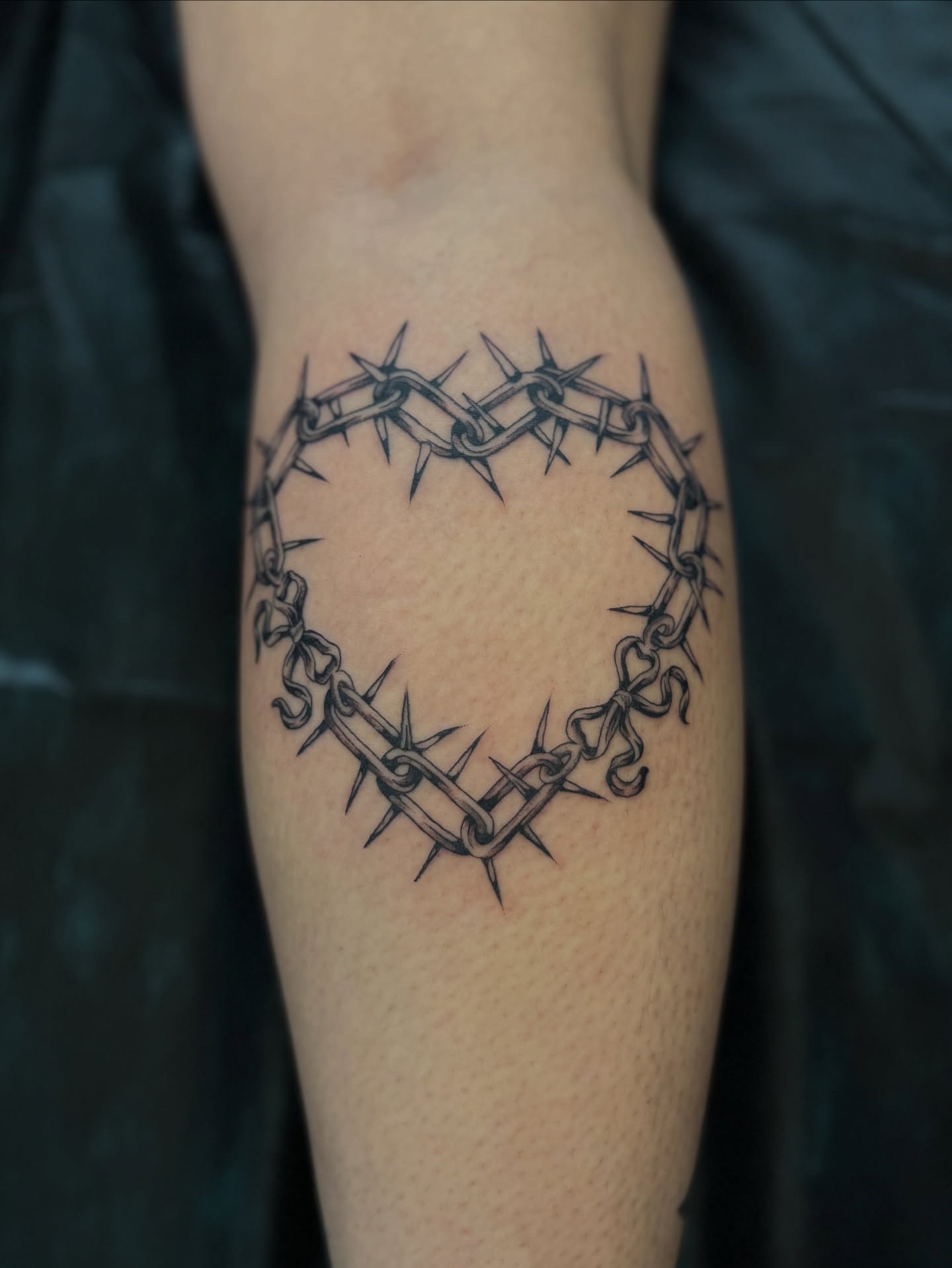 Barbed wire heart black and grey tattoo on the forearm by Sarah Pham