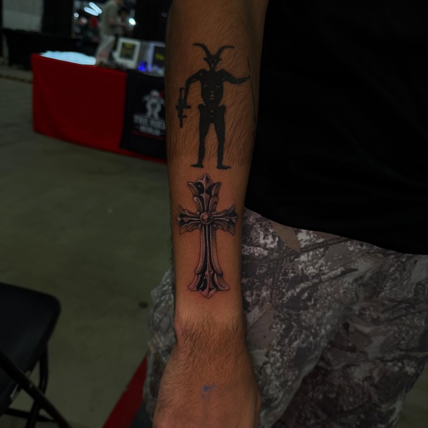 Goat-like figure and cross black and grey tattoo on the forearm by Prncjordn, Stallings, North Carolina