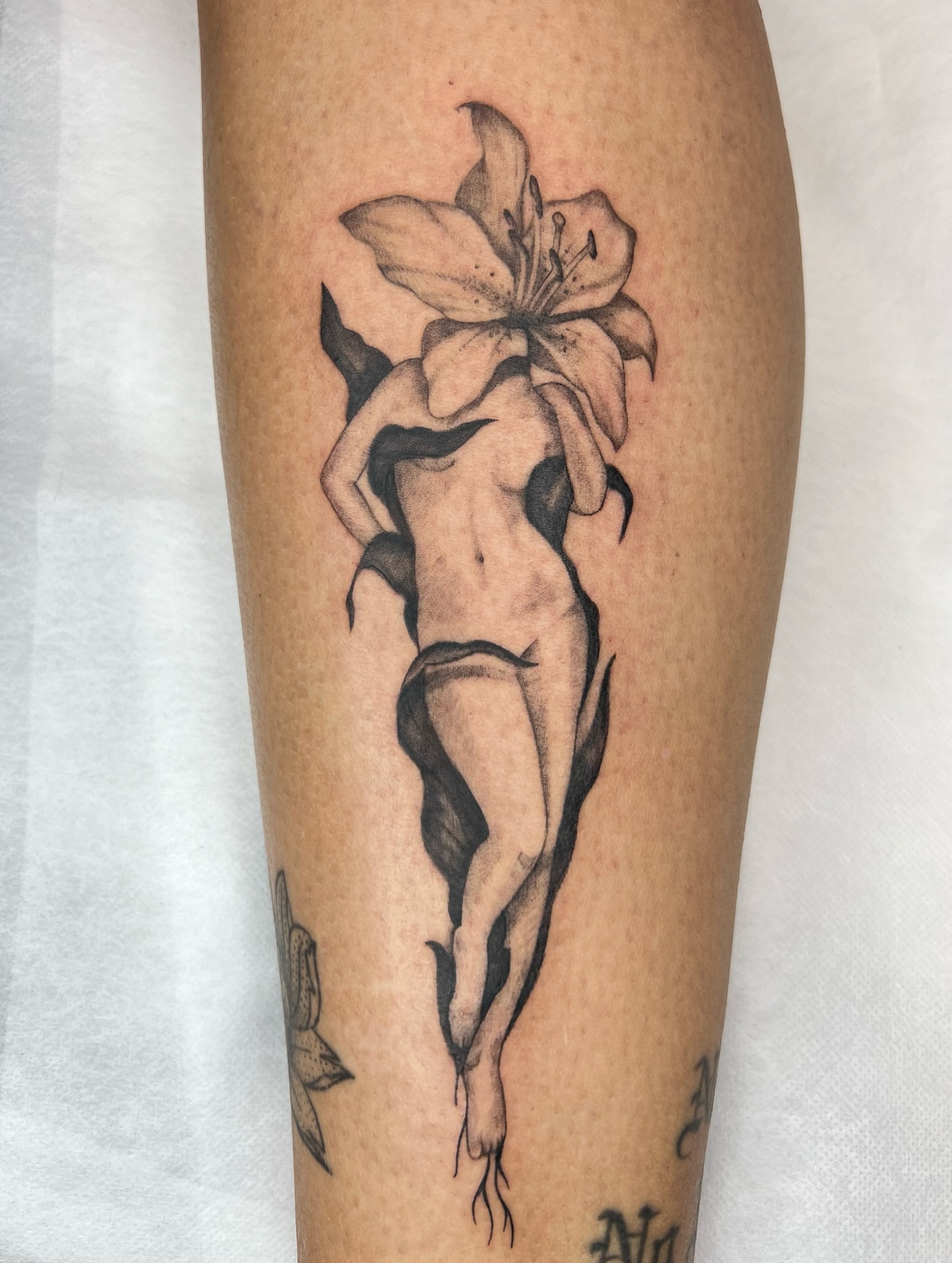 Nude figure with lily realism tattoo on the calf by Red