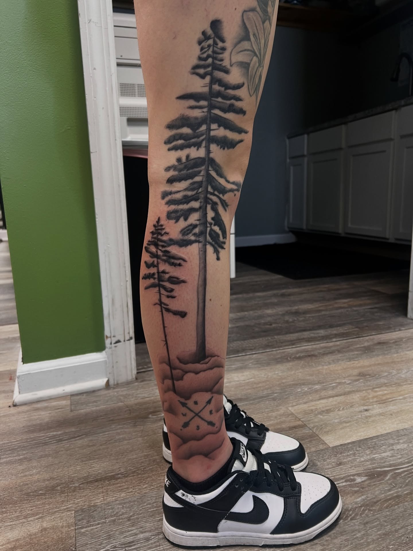 Pine trees black and grey tattoo on the leg by Olivia Suzanne Fada
