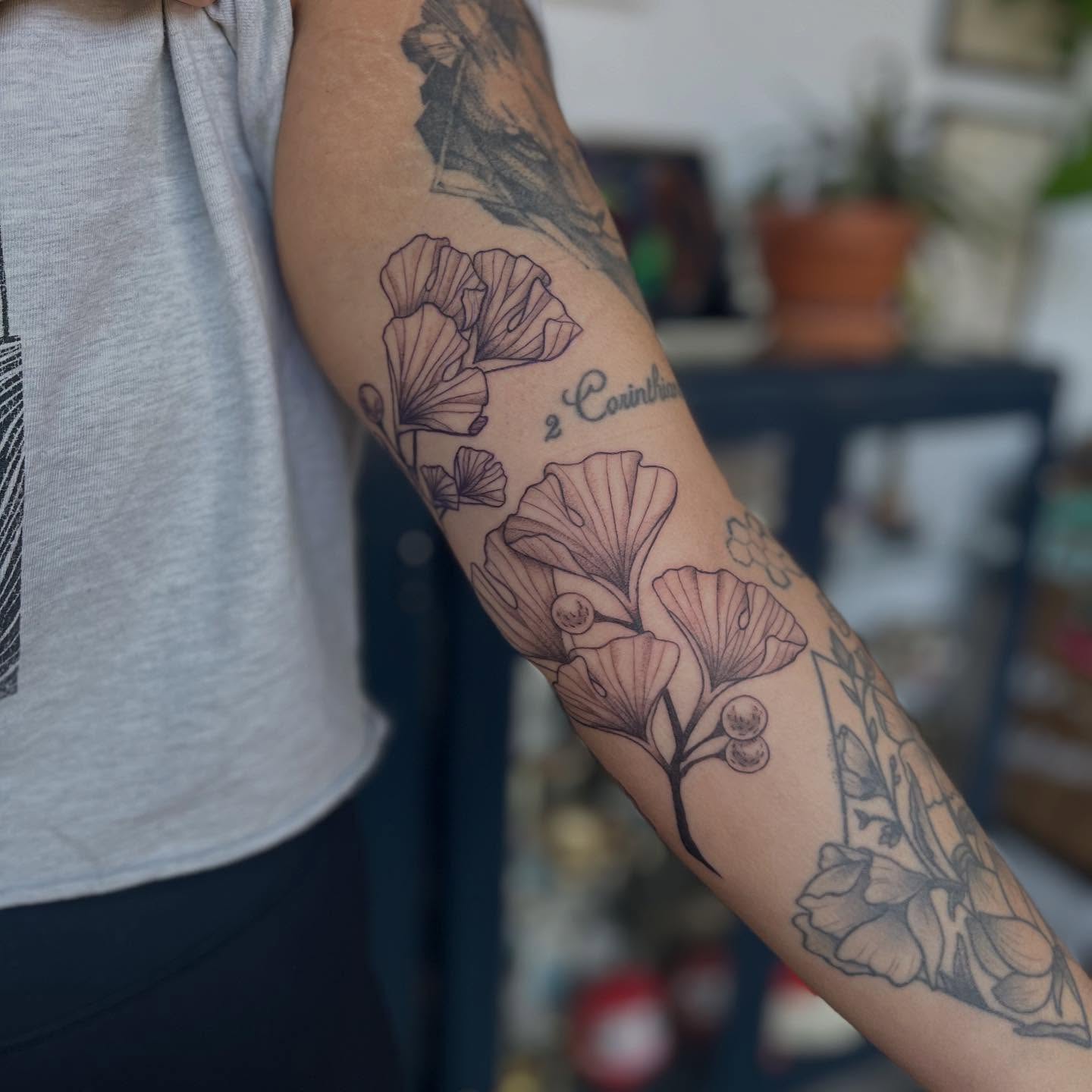Gingko leaves and flowers black and grey tattoo on the forearm by Maddy Anthony