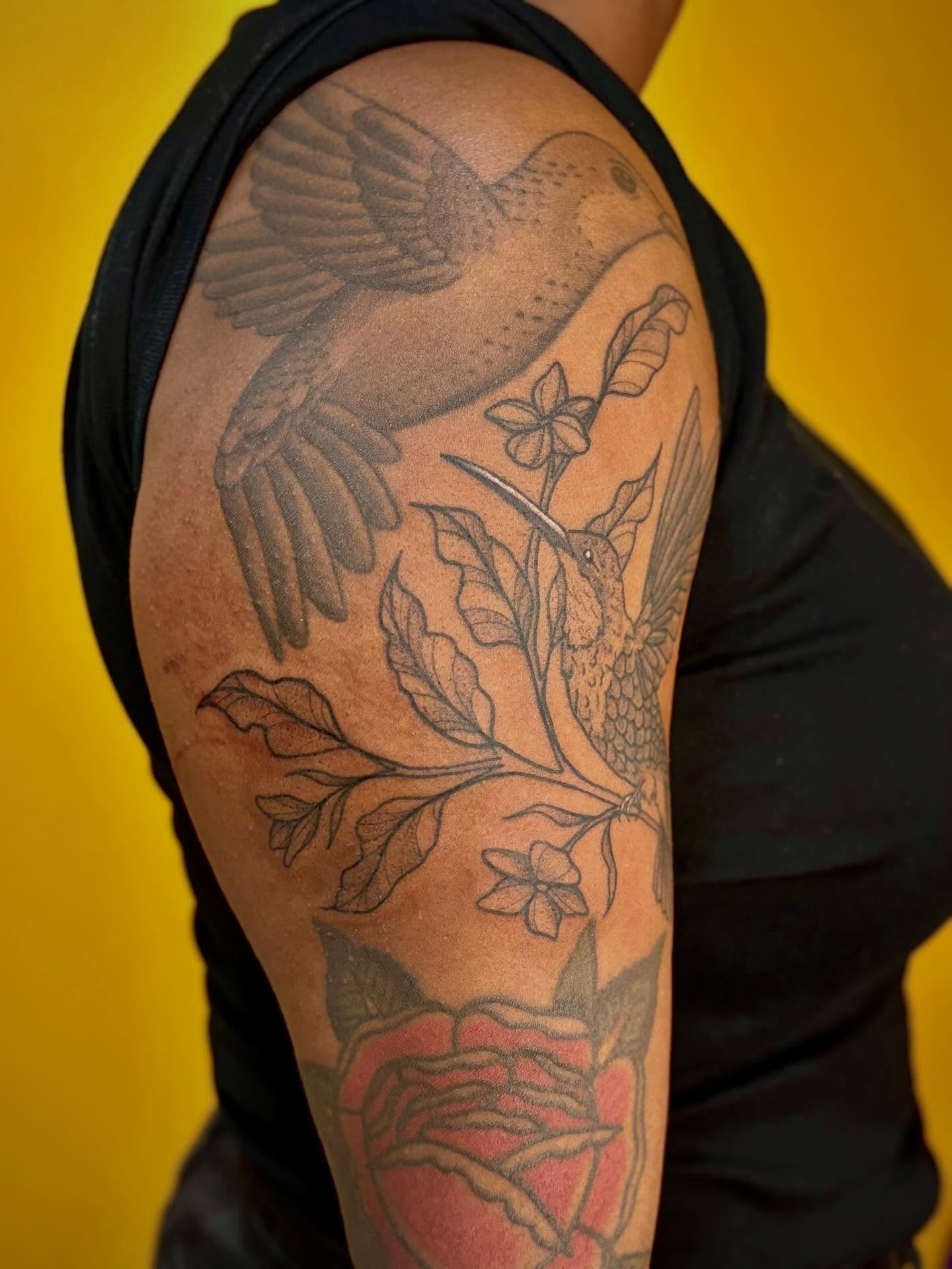 Hummingbird and floral black and grey tattoo on the upper arm by Jazzlyn Hous