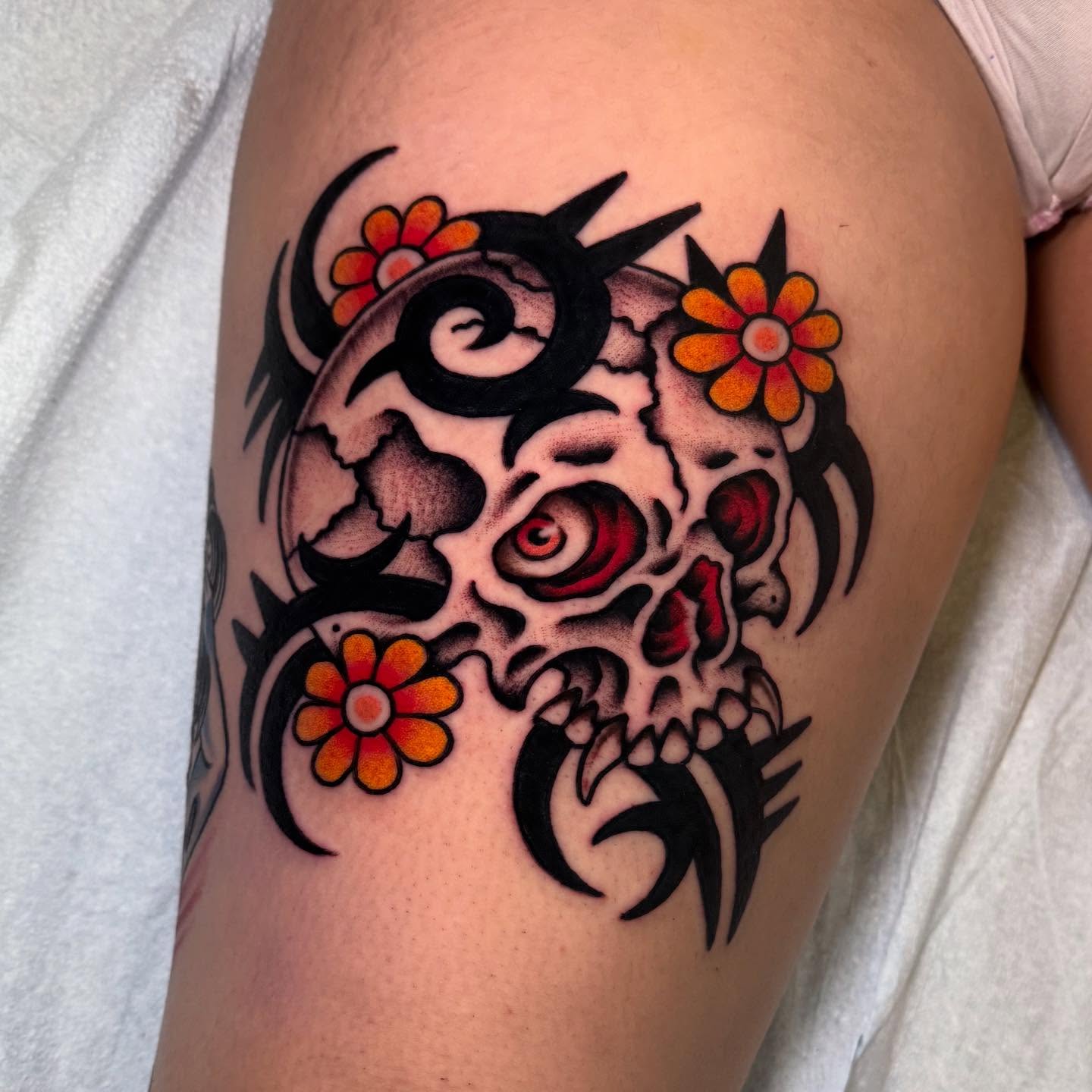 Skull with flowers American traditional tattoo on the thigh by Julia Louise