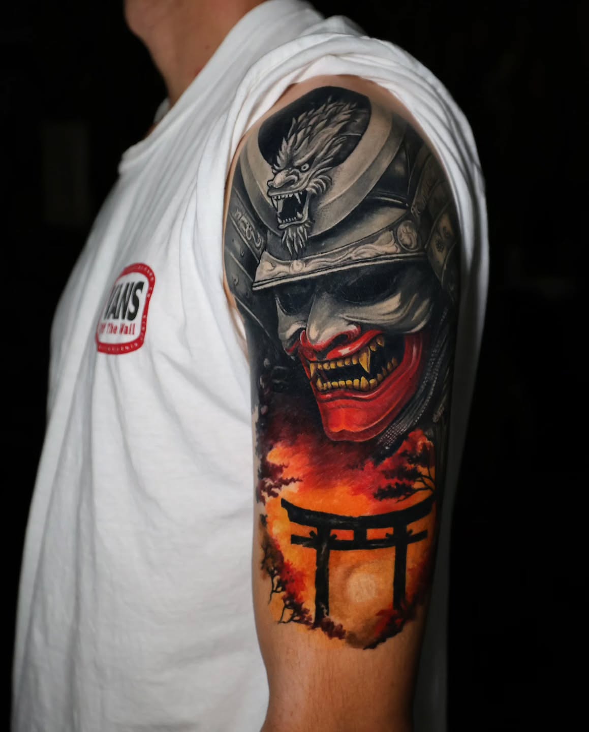 Japanese mask and torii gate dark realism tattoo on the upper arm by Marek Pawlik