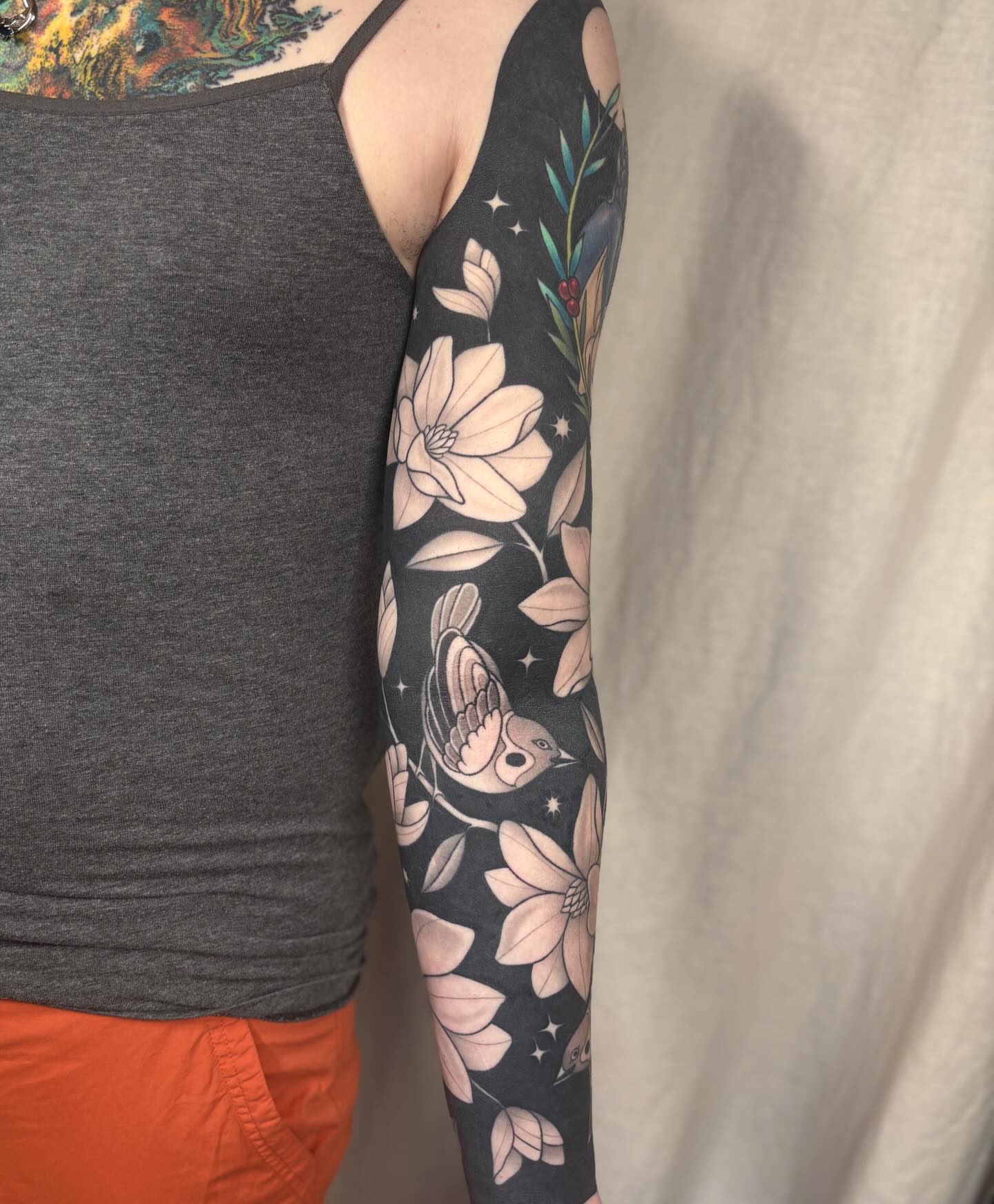 Bird and magnolia flowers new school tattoo on the upper arm by Anna Sage
