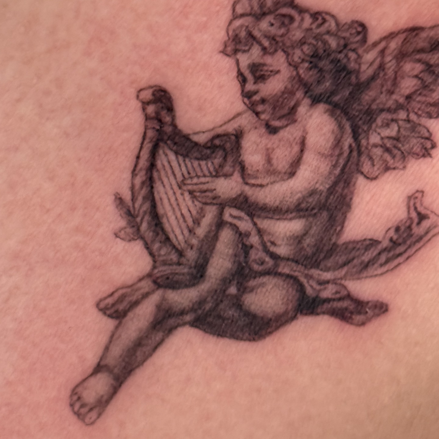 Cherub playing harp black and grey tattoo on the thigh by Brows & Tattoos