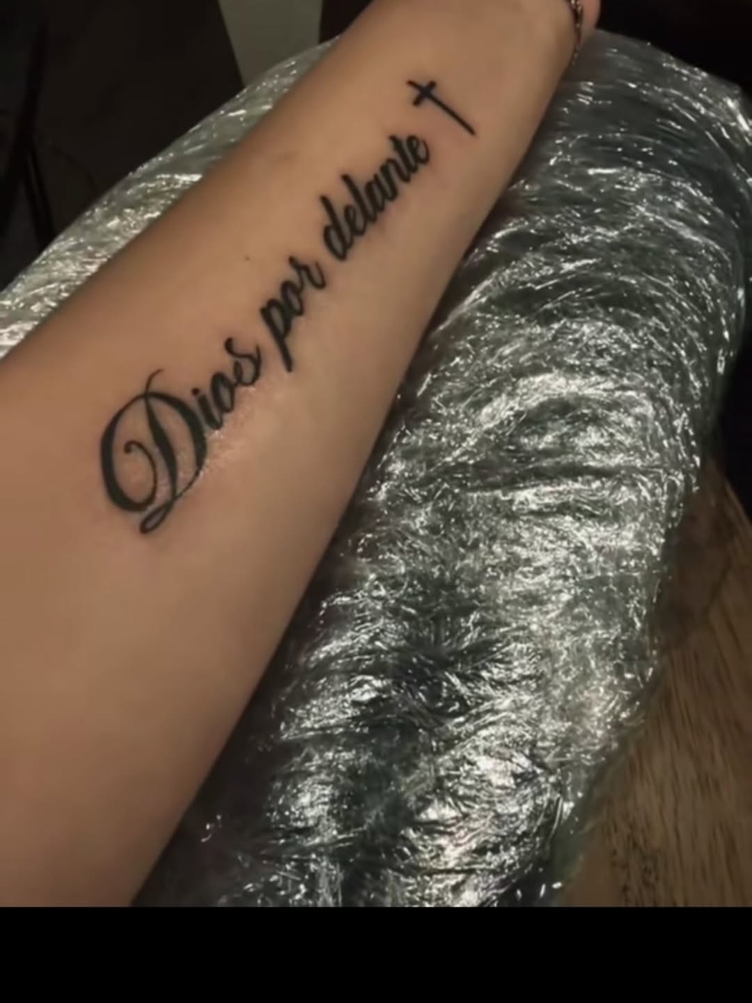 Script lettering with cross lettering tattoo on the forearm by Anna DeLuna