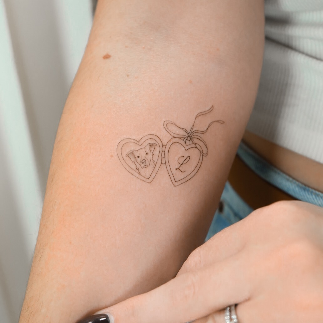 Locket with dog portrait and initial minimalist tattoo on the forearm by Fine Line, New York, New York