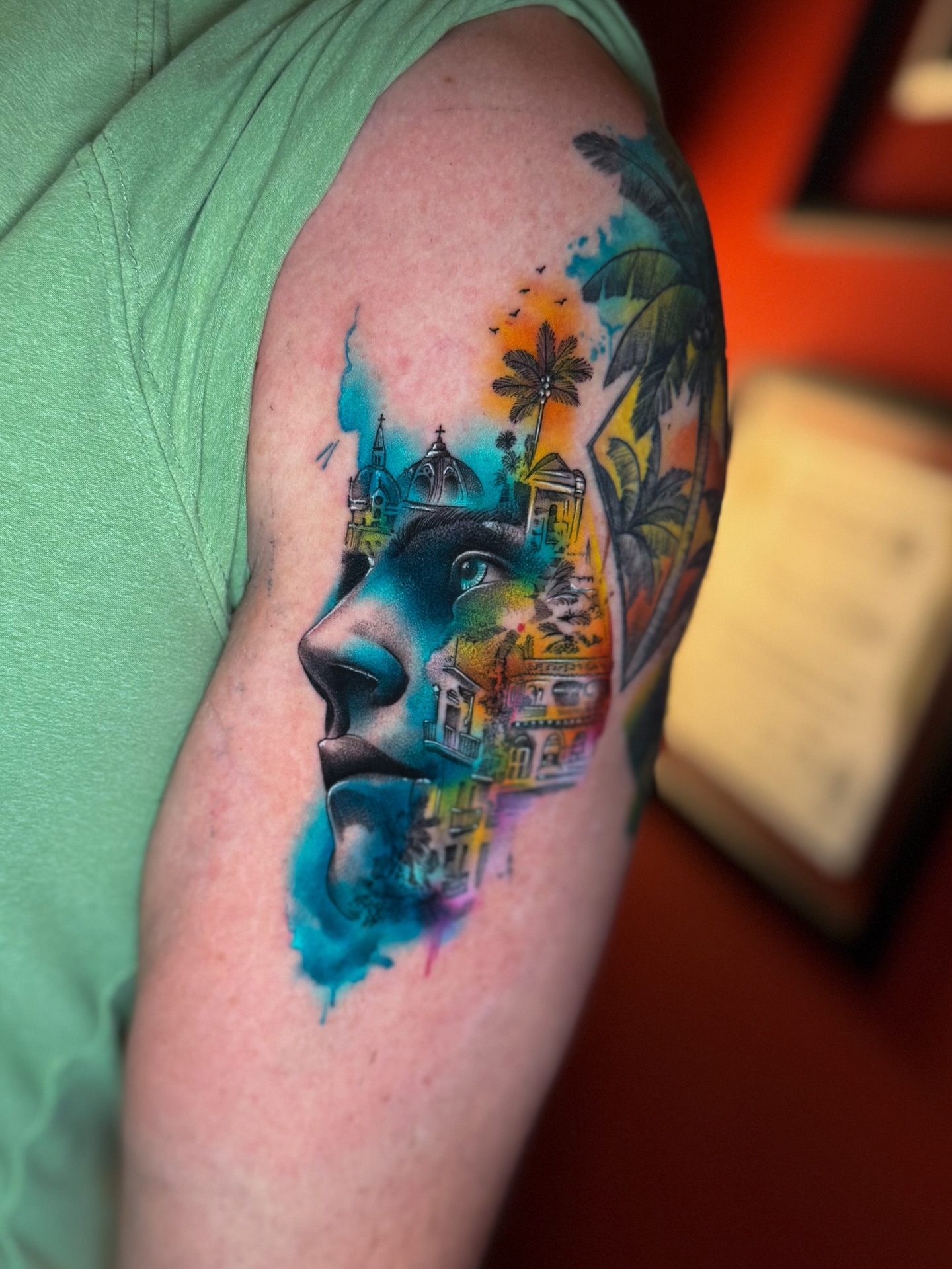 Profile face with cityscape watercolor tattoo on the shoulder by Franz Muñoz