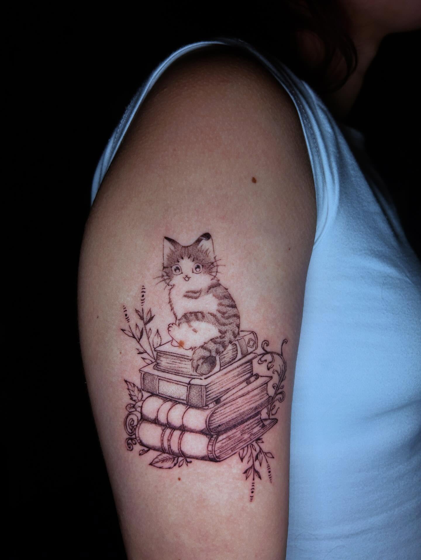 Cat on books realism tattoo on the upper arm by J
