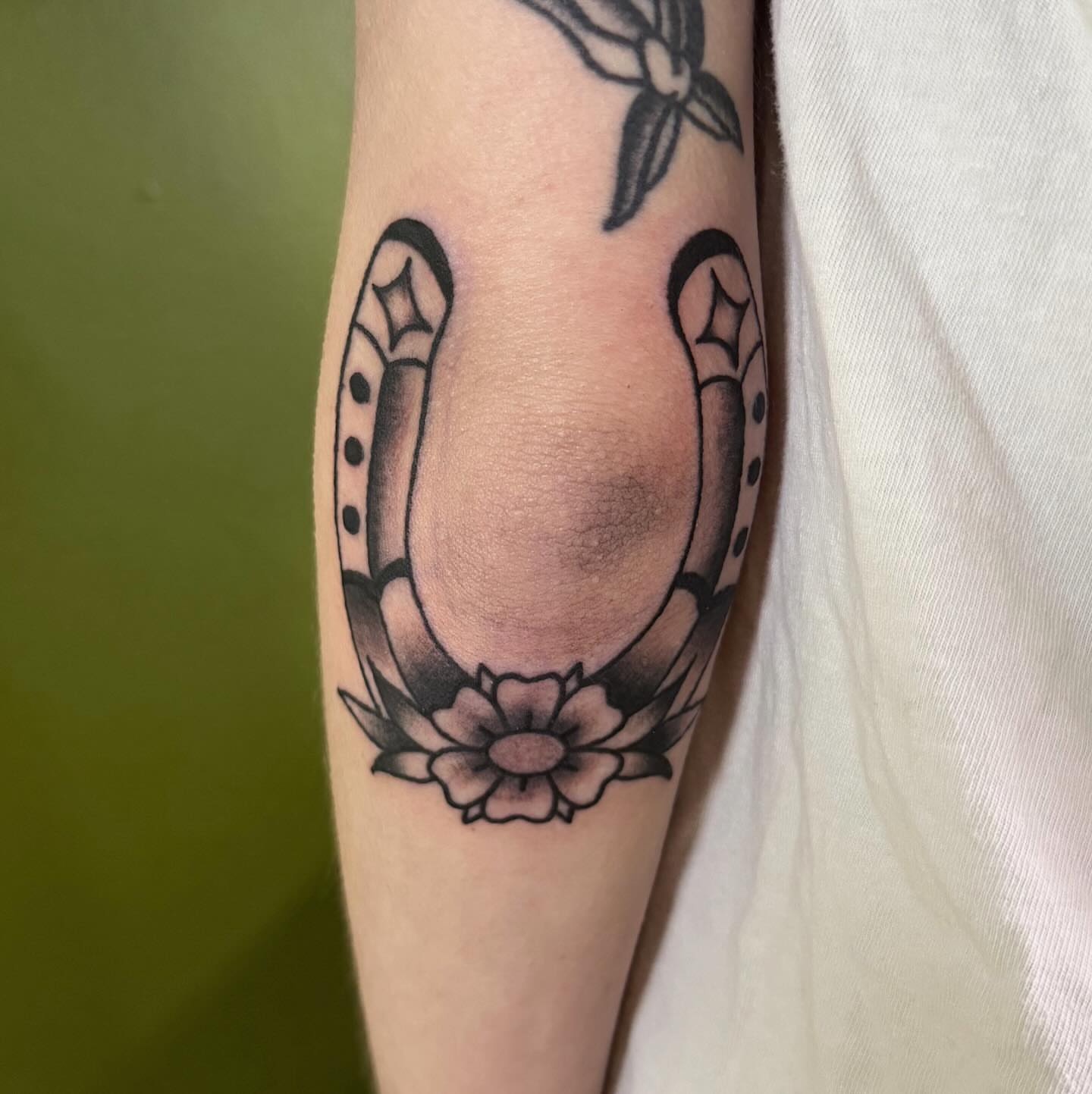 Horseshoe and flower black and grey tattoo on the forearm by 𝕮𝖆𝖘𝖊𝖞 𝕭𝖆𝖘𝖍𝖊𝖗