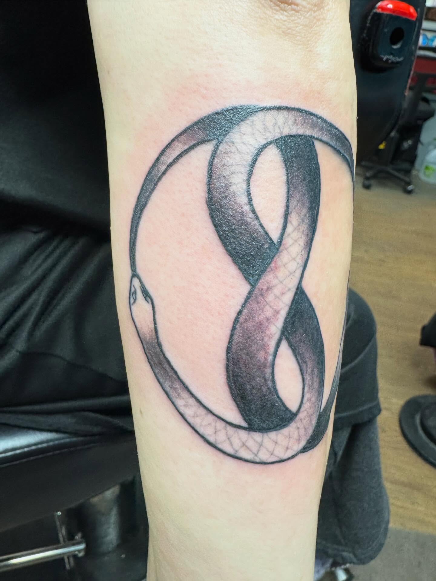 Infinity symbol black and grey tattoo on the forearm by Bob Lindell Tattoos