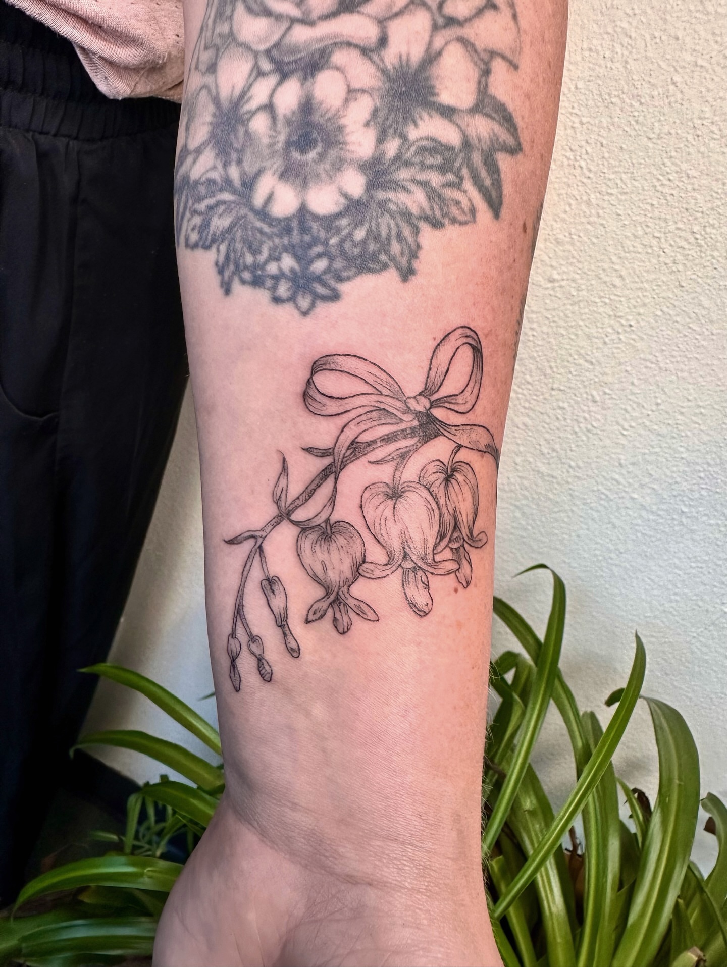 Lily and bow black and grey tattoo on the forearm by kenzie hunter