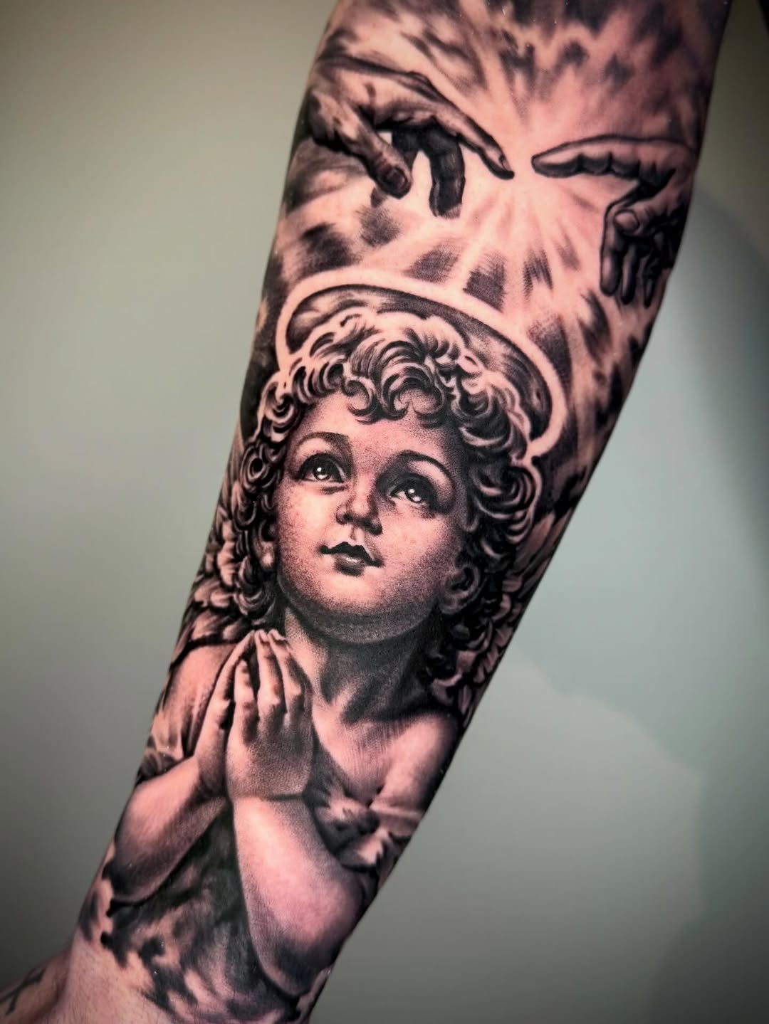 Cherub and hands reaching realism tattoo on the forearm by David Torres