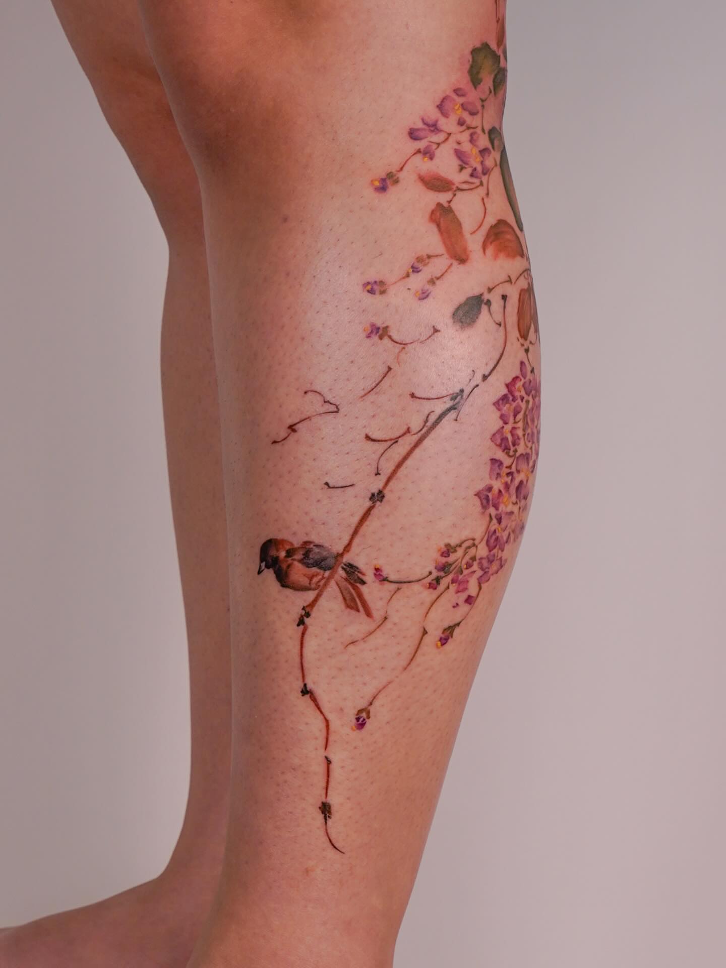 Bird and flowers watercolor tattoo on the calf by Nicki Yến