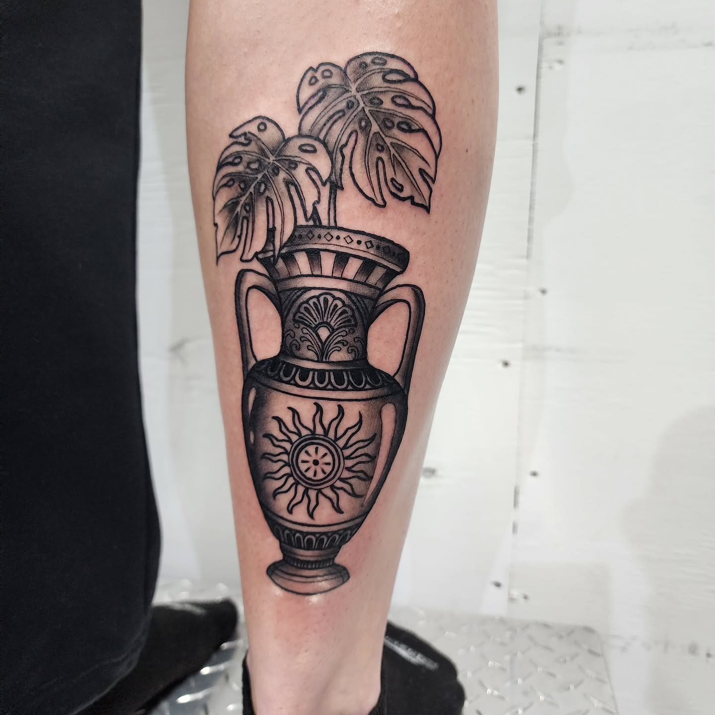 Ancient vase with plant black and grey tattoo on the calf by Robert Glover