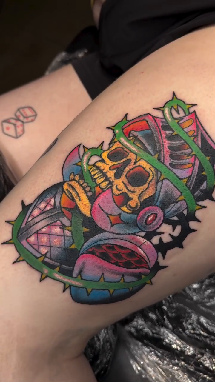 Skull with headphones and thorny vines American traditional tattoo on the thigh by Mercy Dean