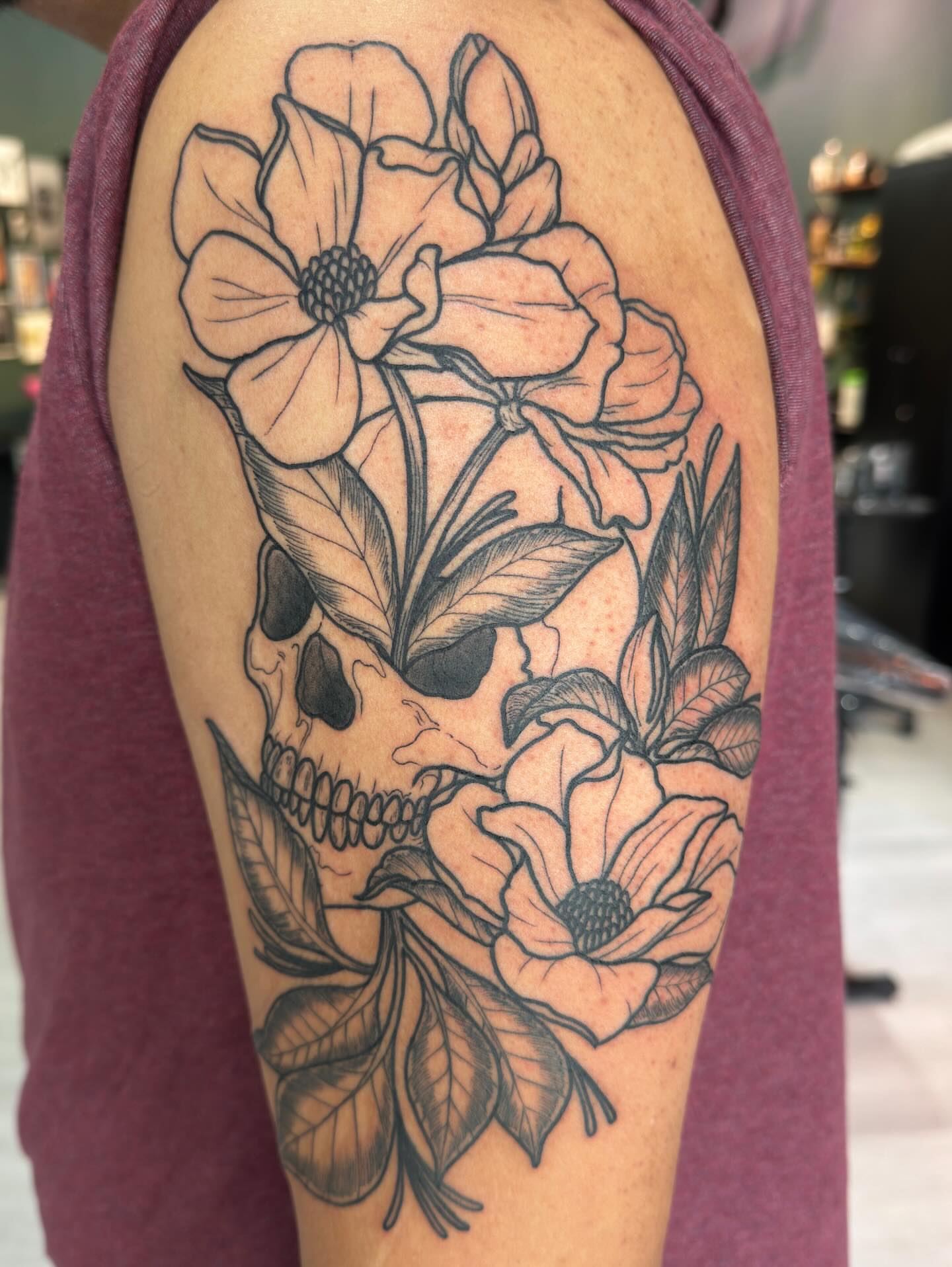 Skull and flowers black and grey tattoo on the upper arm by Patrick Carroll