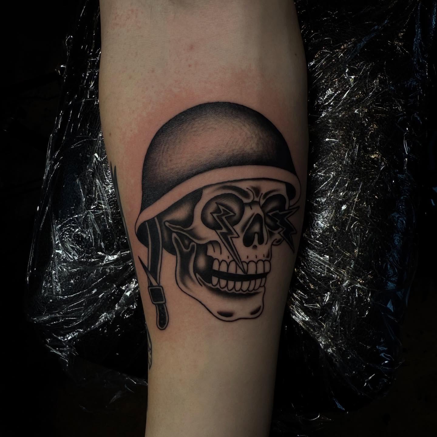 Skull wearing helmet black and grey tattoo on the forearm by frankie quadrini