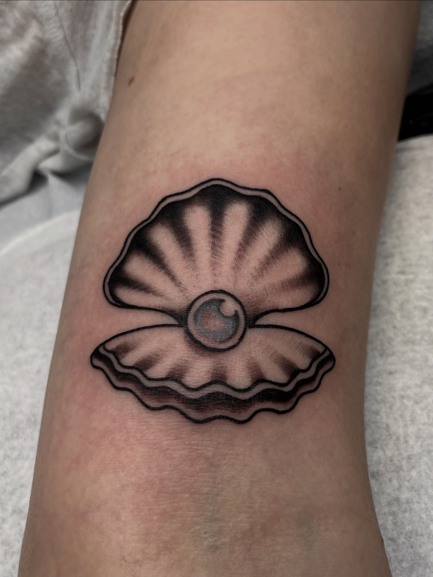 Scallop shell black and grey tattoo on the forearm by Macy Bird