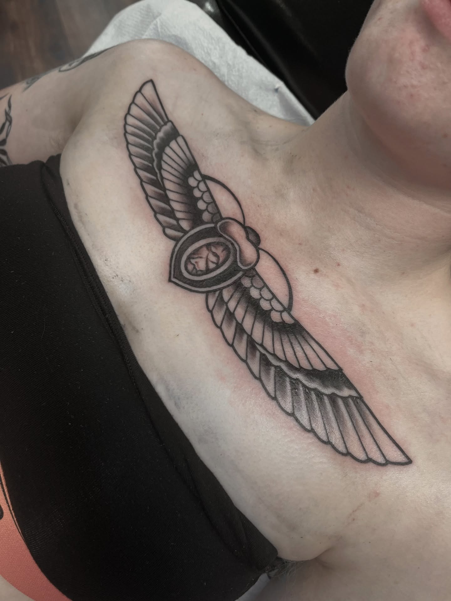 Winged shield black and grey tattoo on the chest by Macy Bird