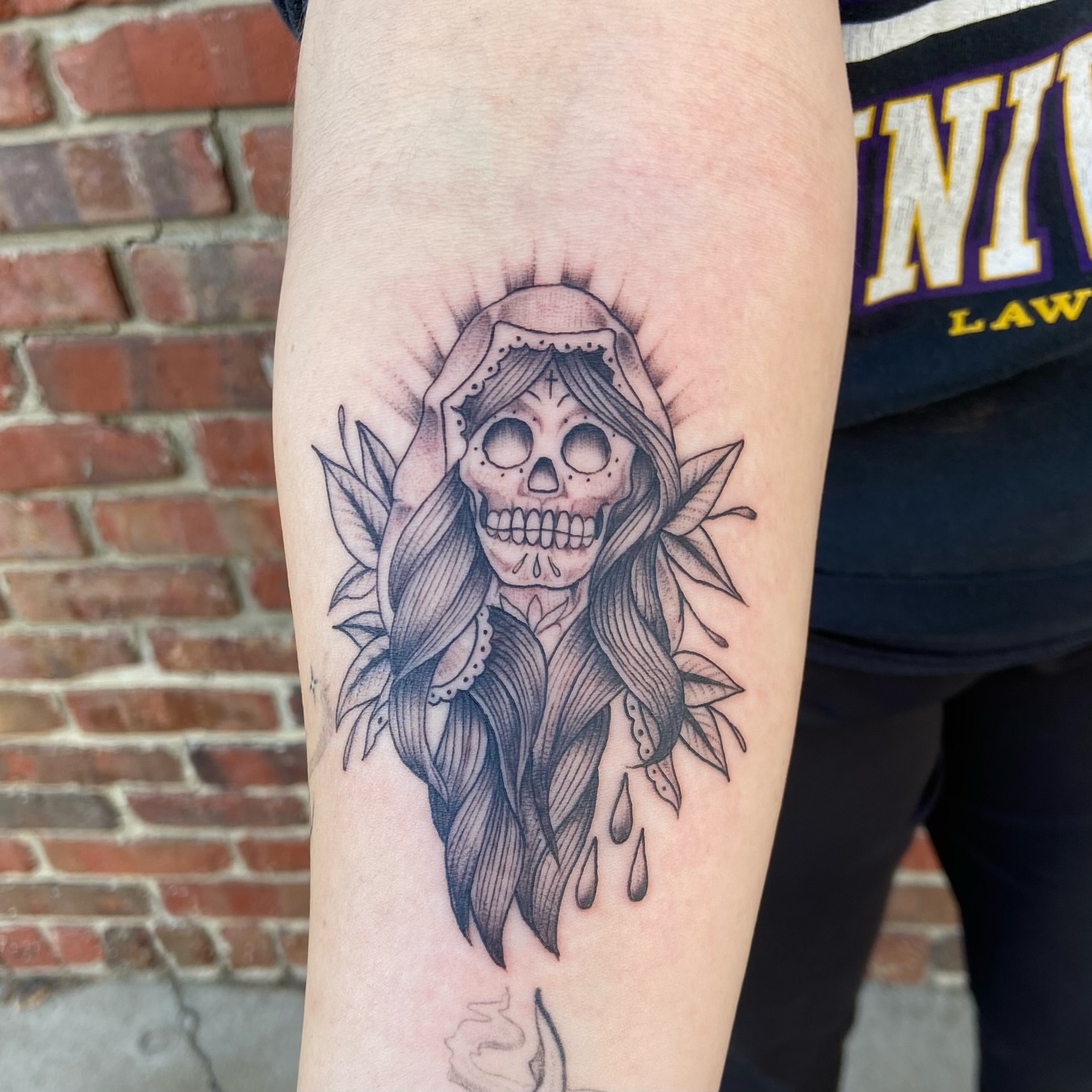 Skull with long hair black and grey tattoo on the forearm by Anthony Robles