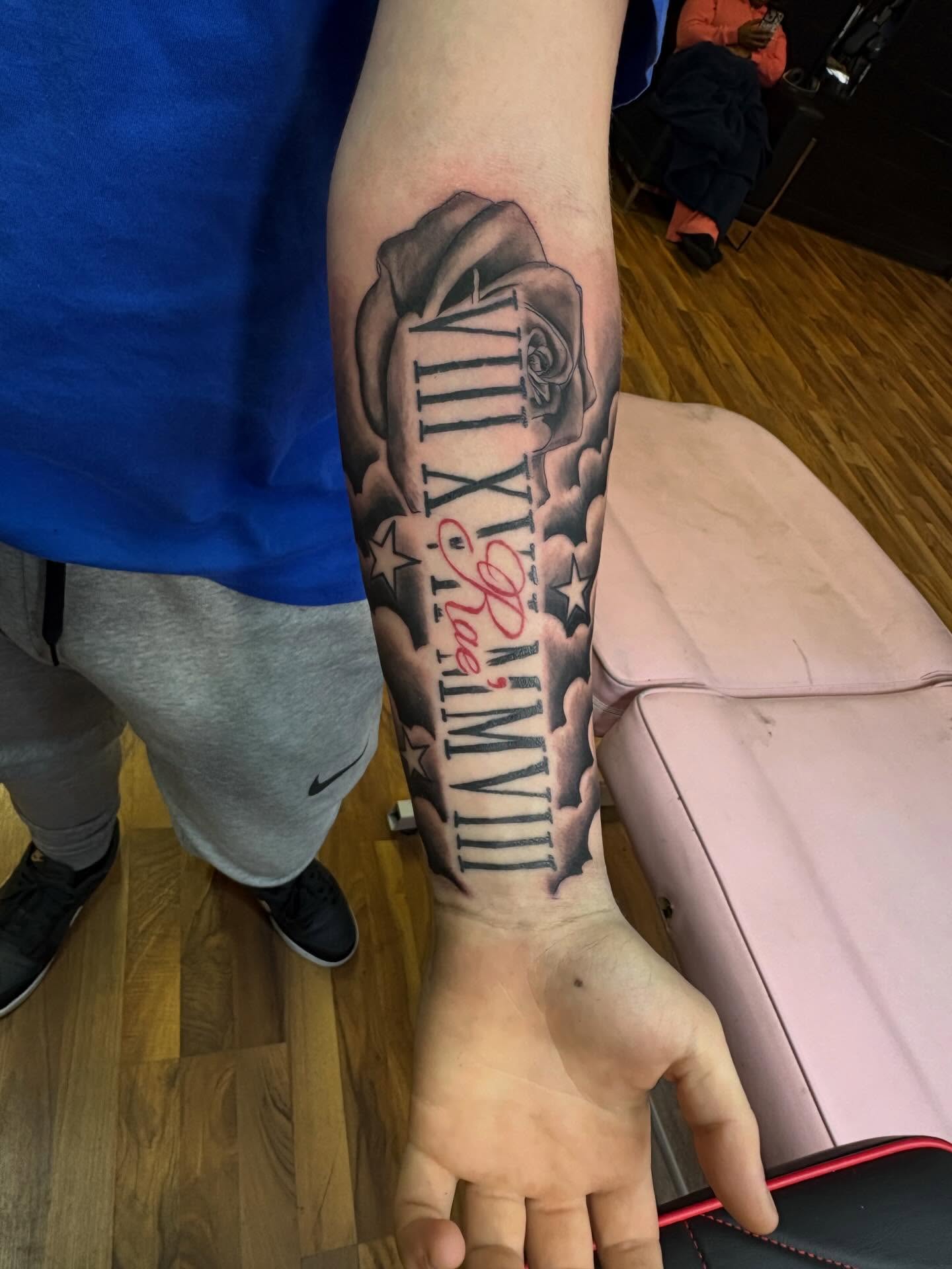 Roman numerals and rose black and grey tattoo on the forearm by 𓂀 𝕊ℍ𝔼𝕃𝕃𝕐 𓂀