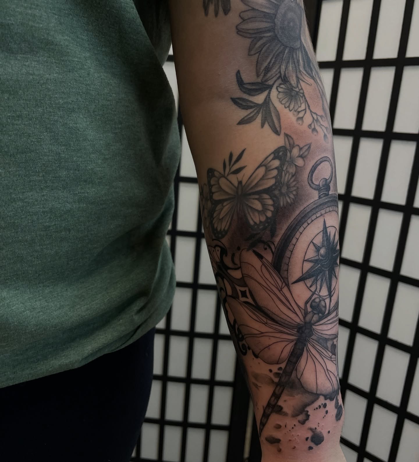 Butterfly, compass, dragonfly, flowers black and grey tattoo on the forearm by kaylee