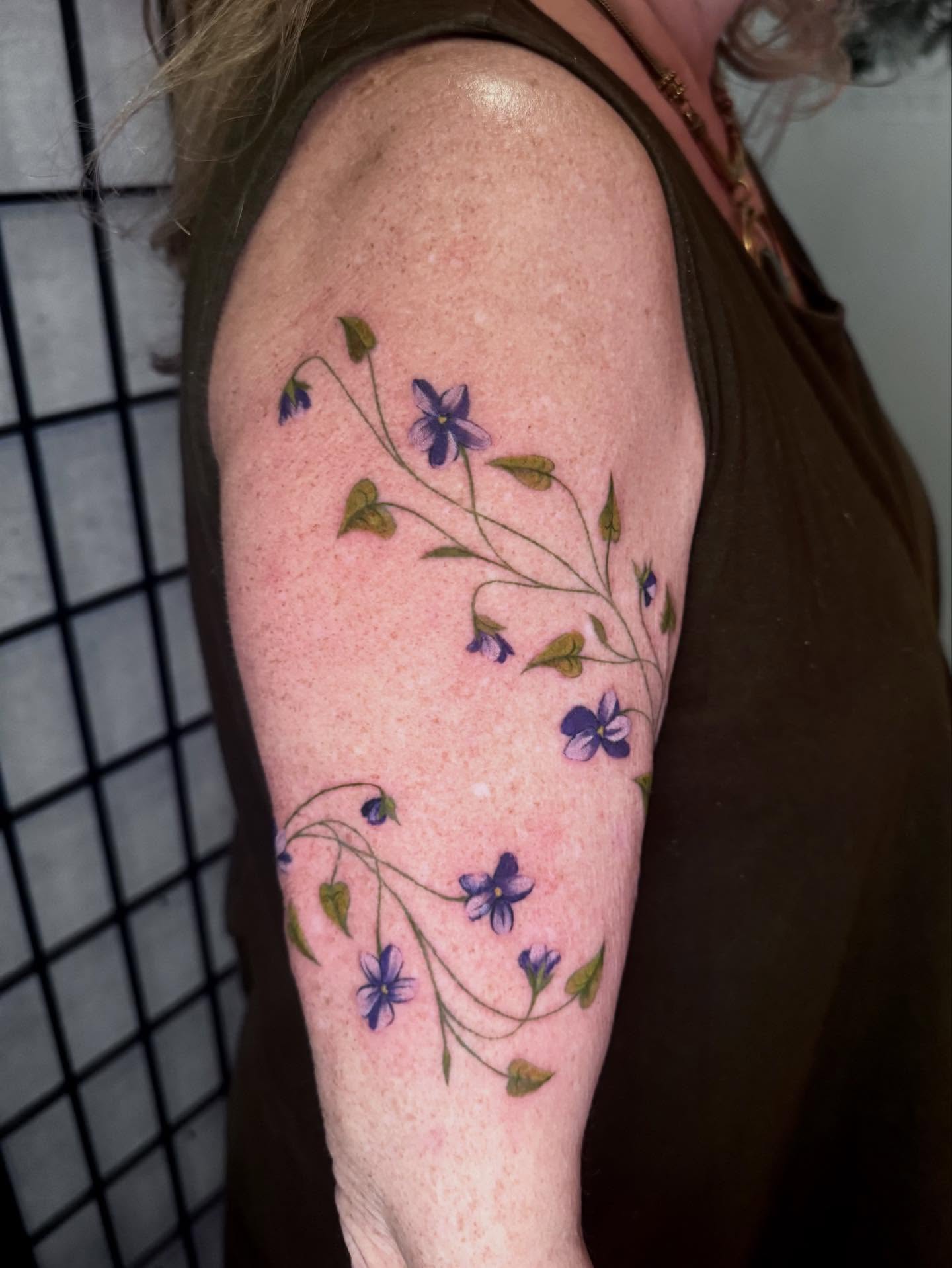 Purple flowers watercolor tattoo on the upper arm by Morgan Peeples