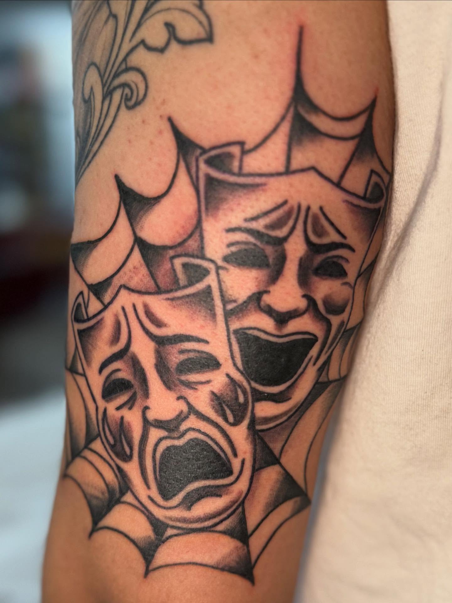 Theatrical masks black and grey tattoo on the forearm by Rigo Vargas