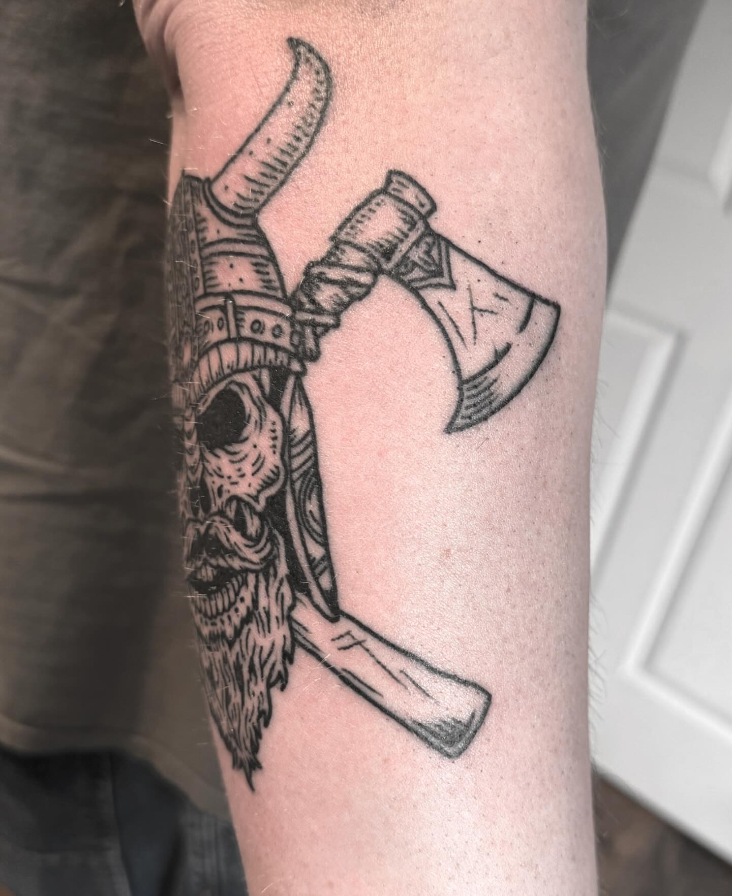 Viking helmet and axe black and grey tattoo on the forearm by Joe Truck