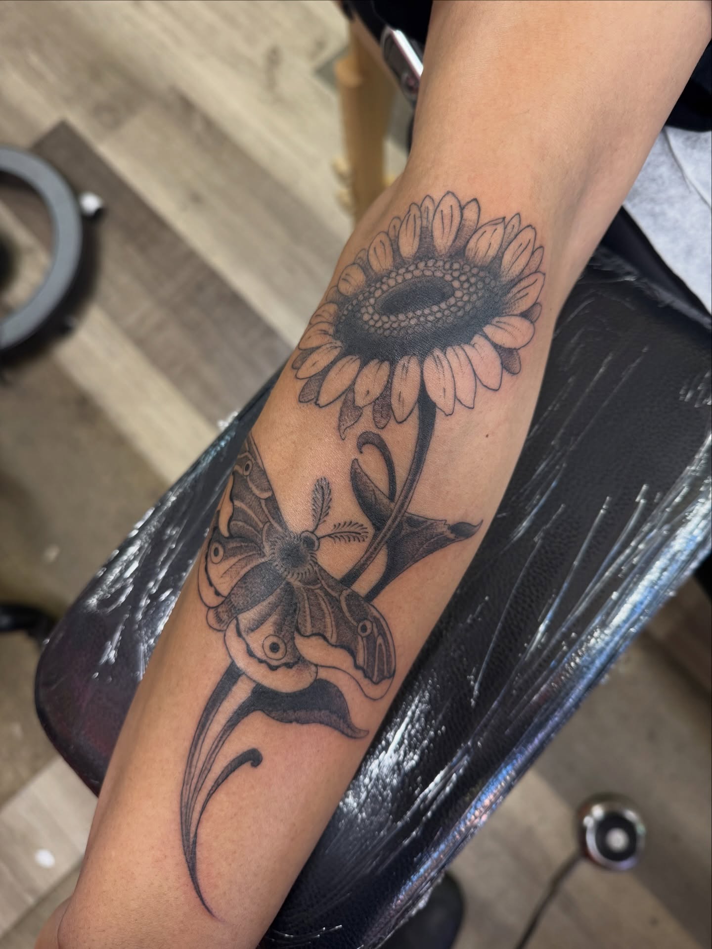 Sunflower and moth black and grey tattoo on the forearm by Chris Orta
