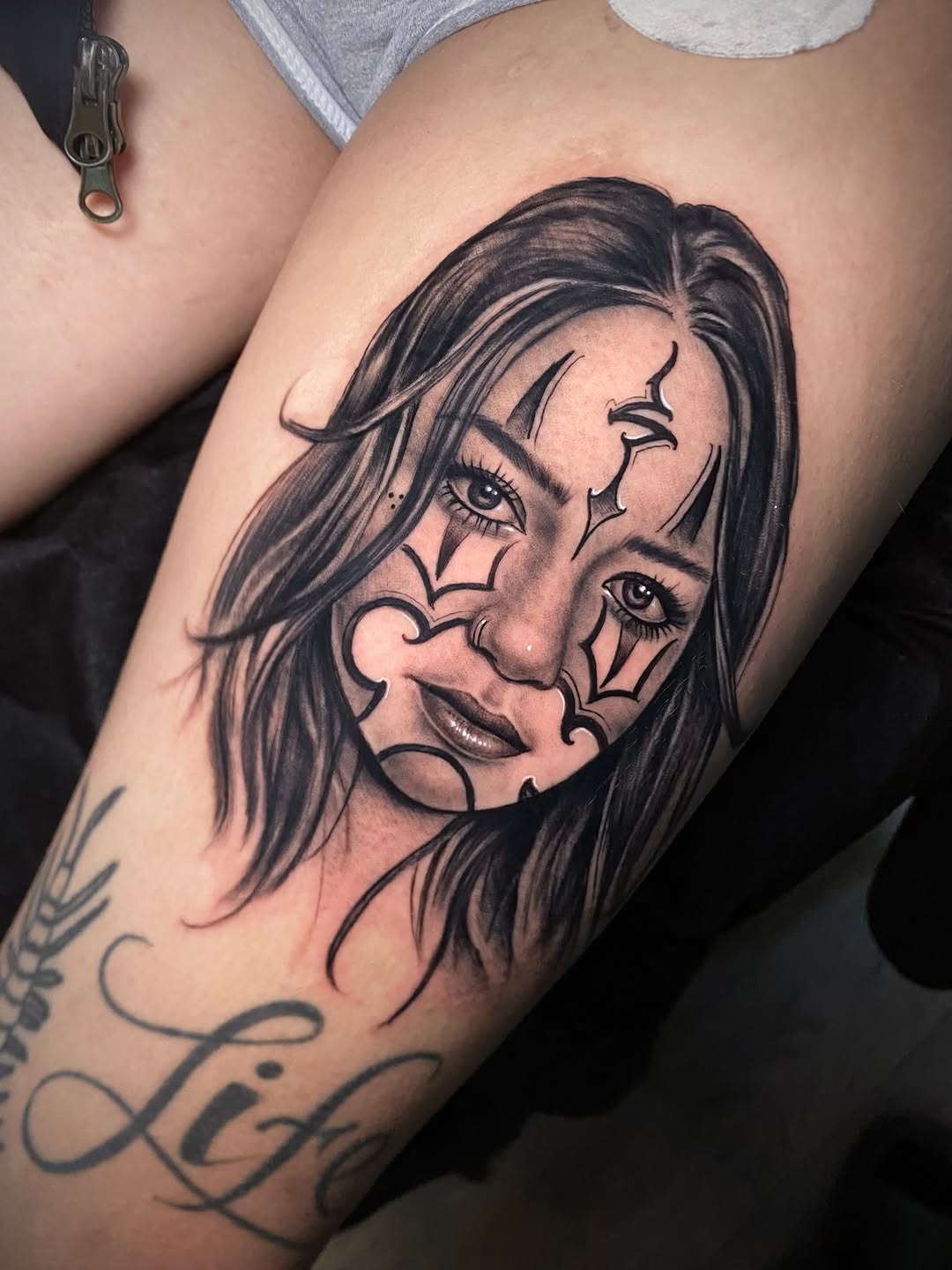 Woman's face with clown makeup Chicano tattoo on the thigh by Adam Newton