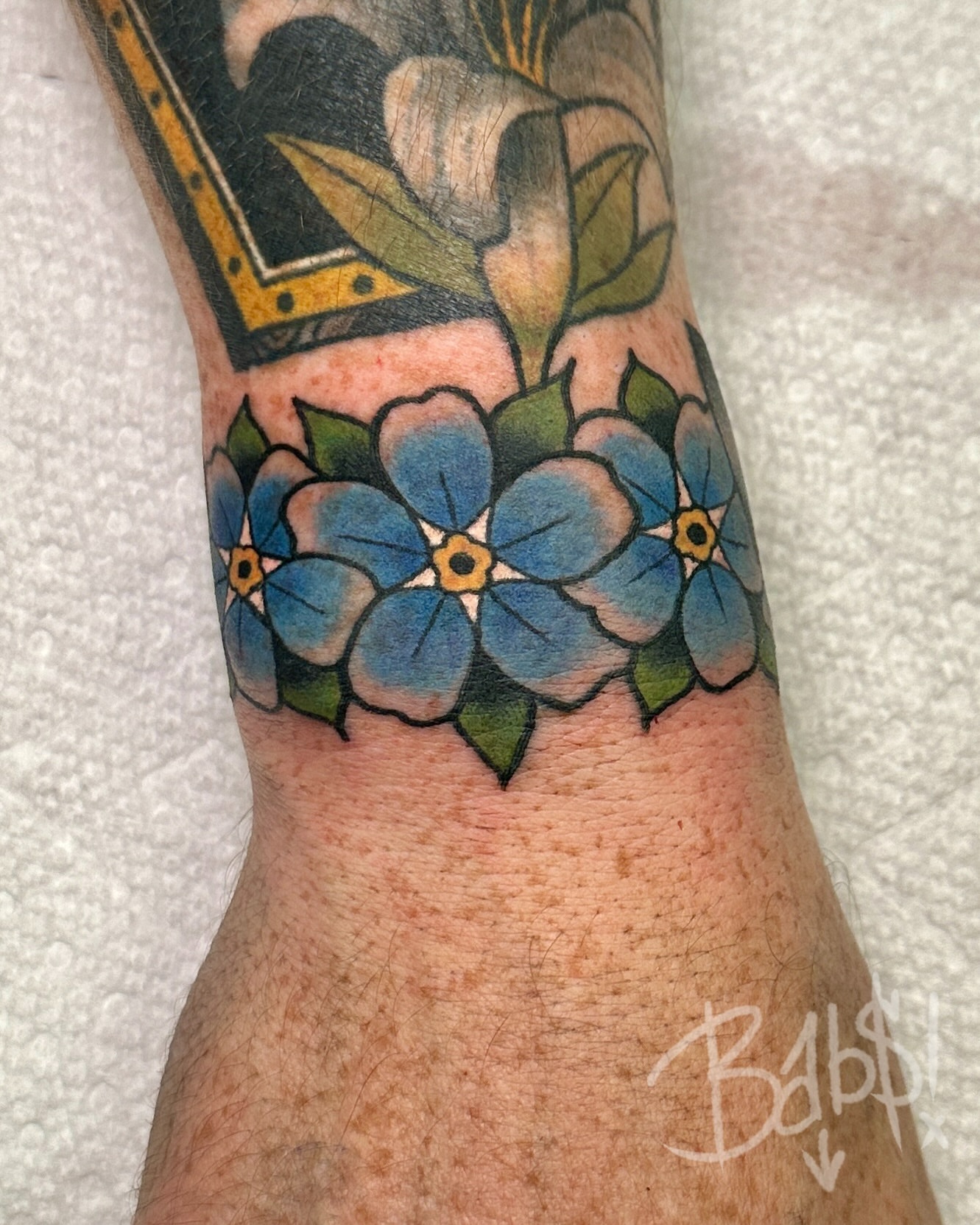 Blue forget-me-not flowers American traditional tattoo on the forearm by Justin B