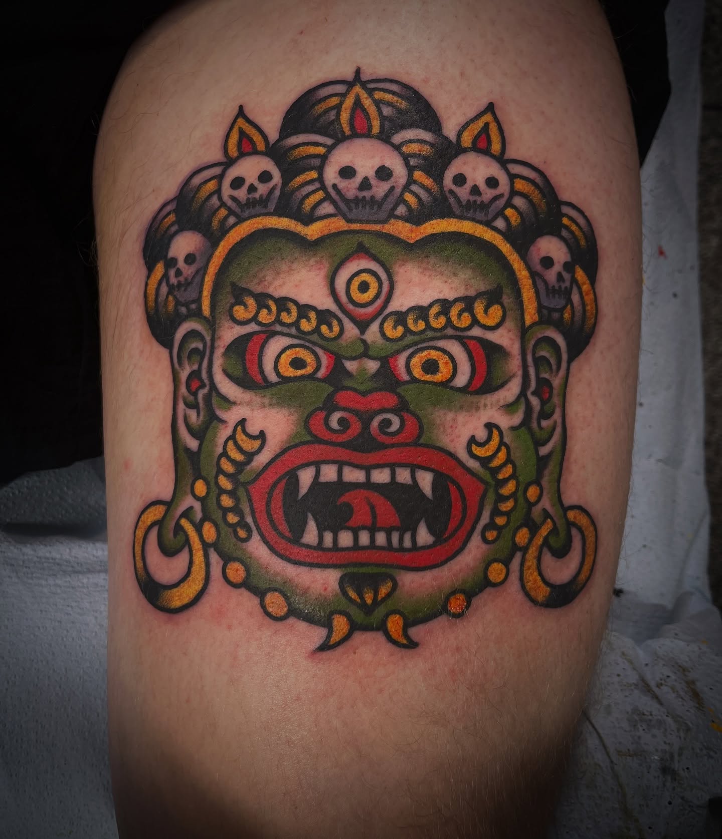 Mask with skulls American traditional tattoo on the thigh by Deya Aven, Nashville, Tennessee